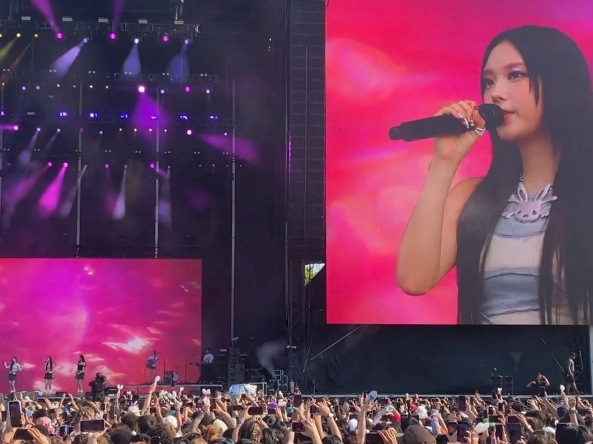 Concert with a large crowd, stage lights, and a big screen displaying a female singer holding a microphone during a performance.