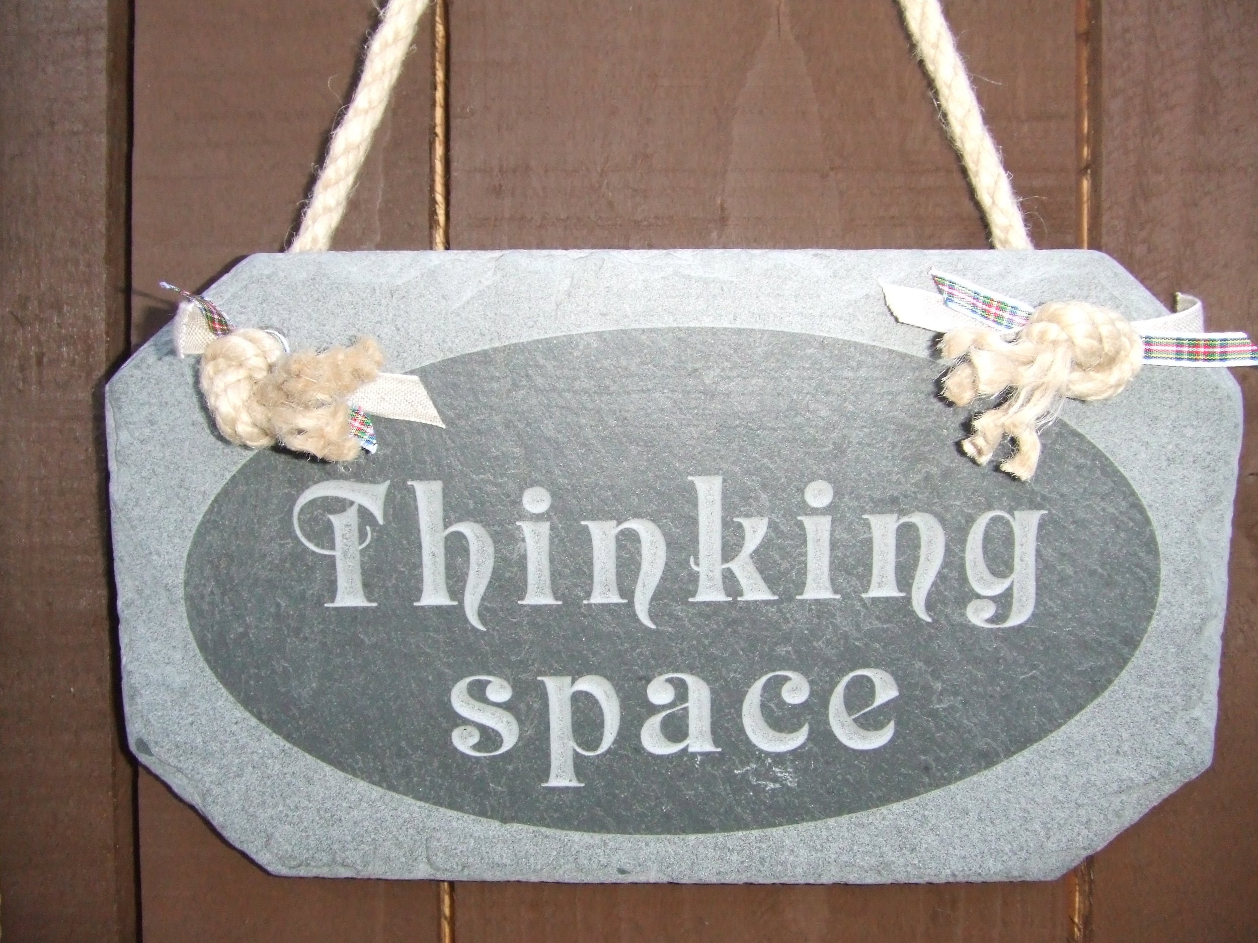Gray slate sign with 'Thinking space' text hanging on a wooden background.