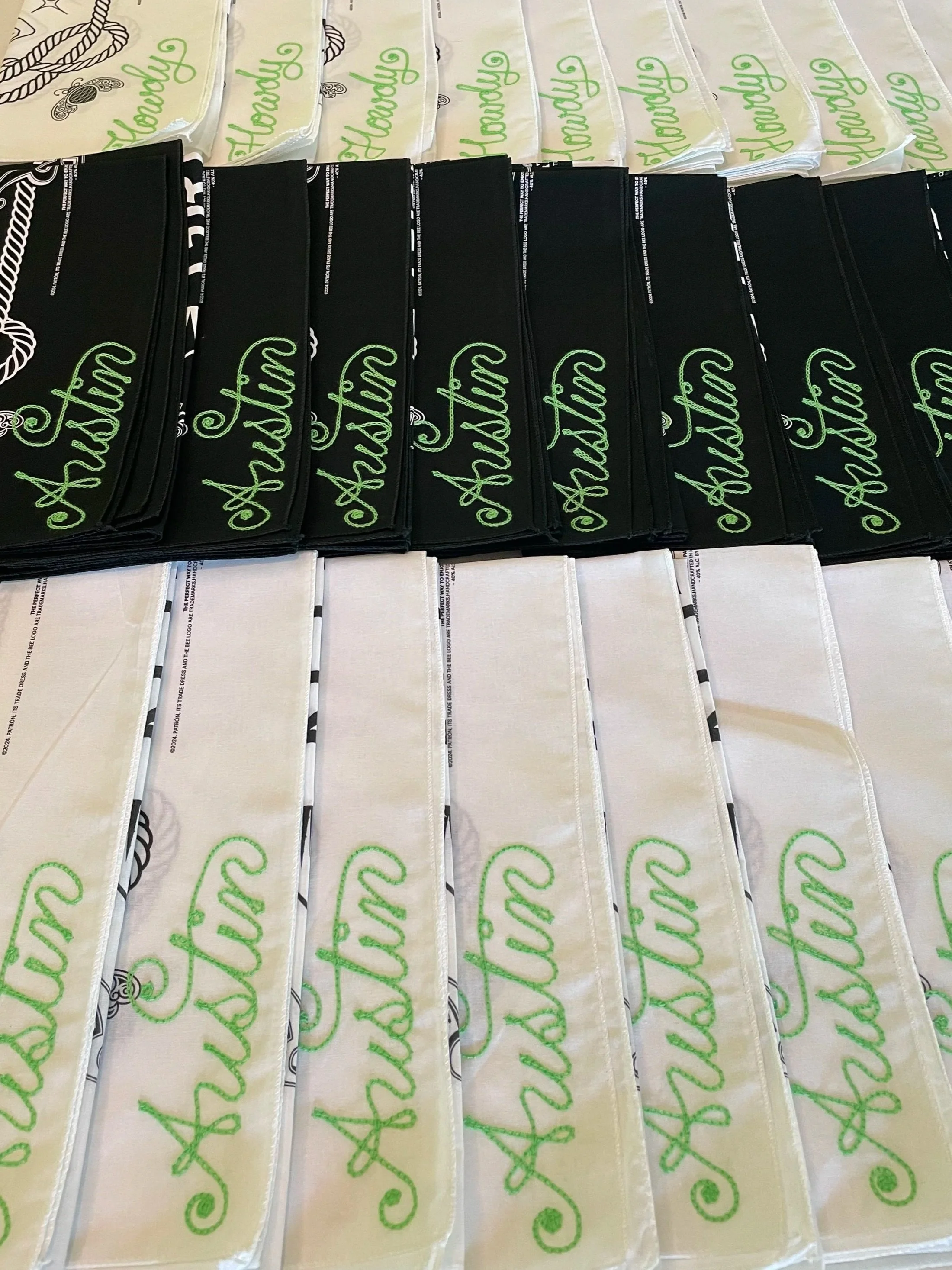 A display of various cloth bandanas with embroidered names, including white and black bandanas, lined up in rows. Double Vision was on-site to provide live embroidery for guest at the Rolling Stone and Patron ACL event in Austin, Texas