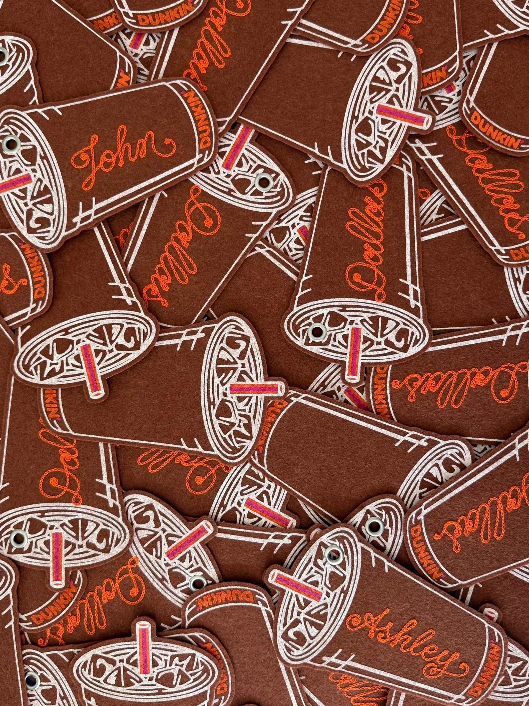 Multiple felt keychains tags designed to look like Dunkin' cups, with names written on them, such as 'John,' 'Dallas,' and 'Ashley.'