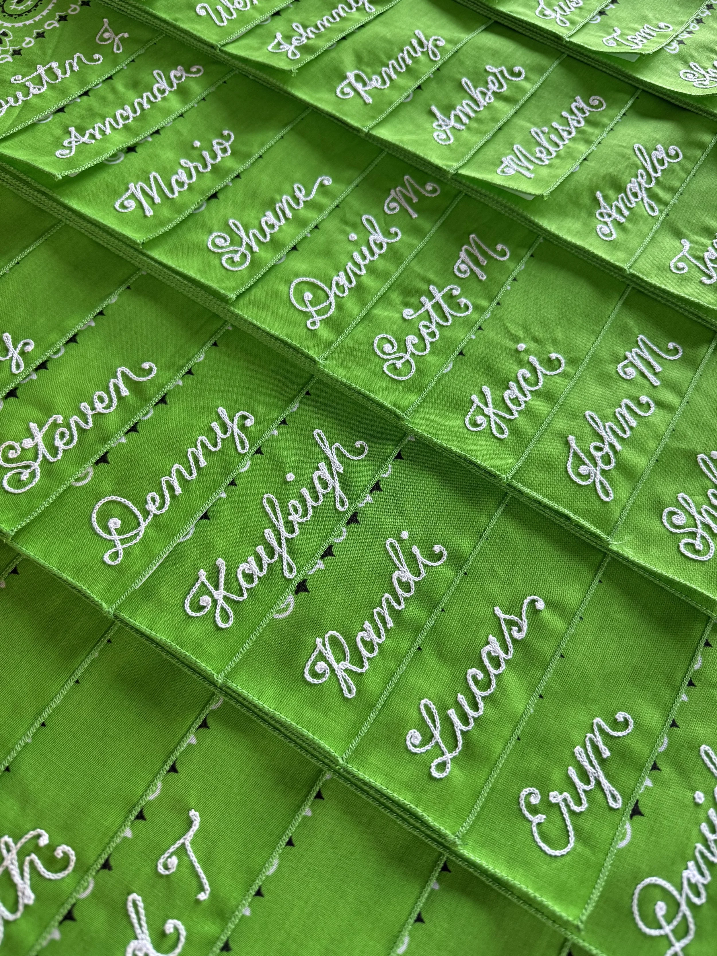 Bulk bandana order with chainstitch embroidered names. Green bandanas, white thread.