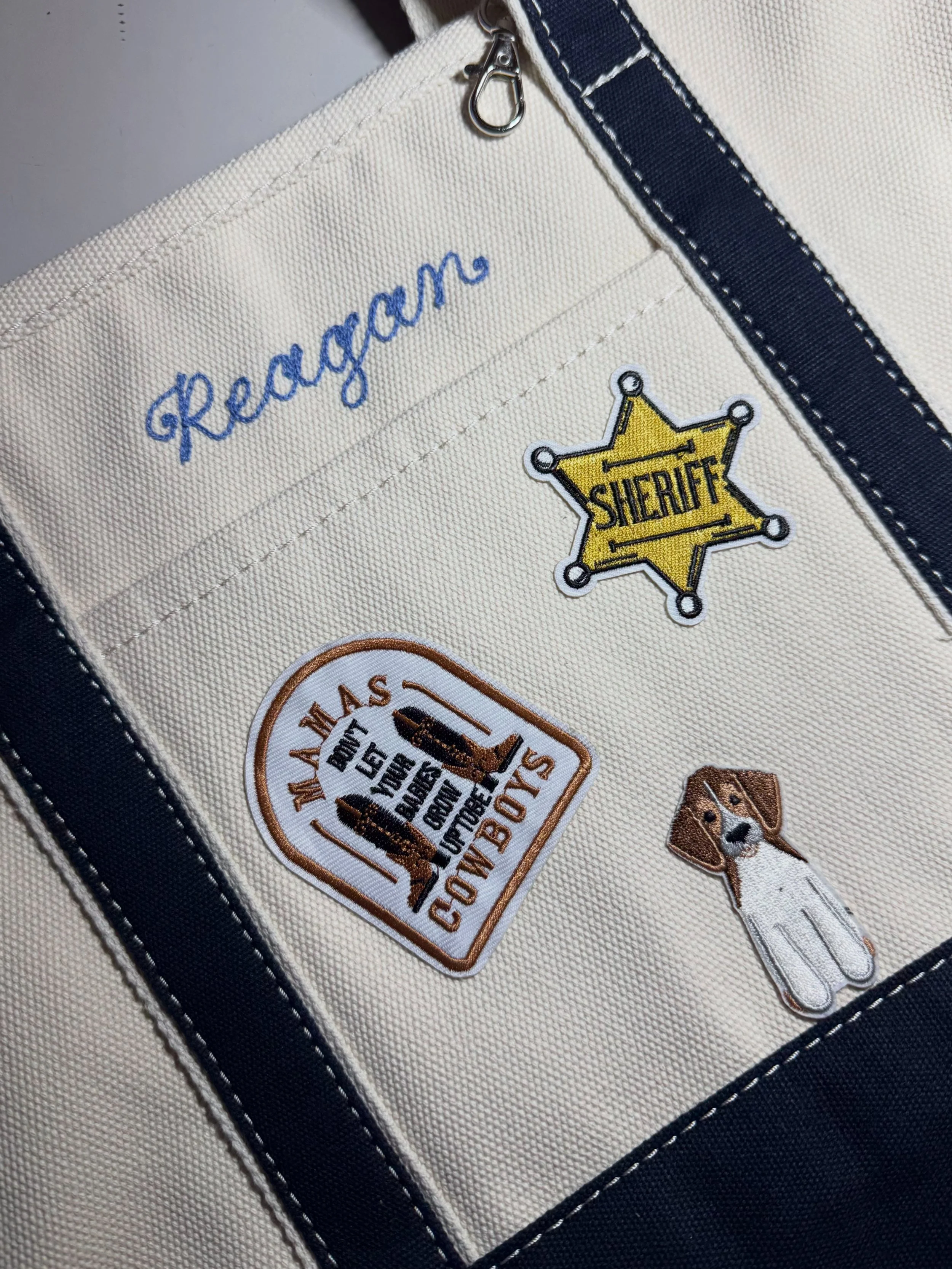 Close-up of a beige fabric tote with patches including a sheriff badge, a dog patch, and a patch.