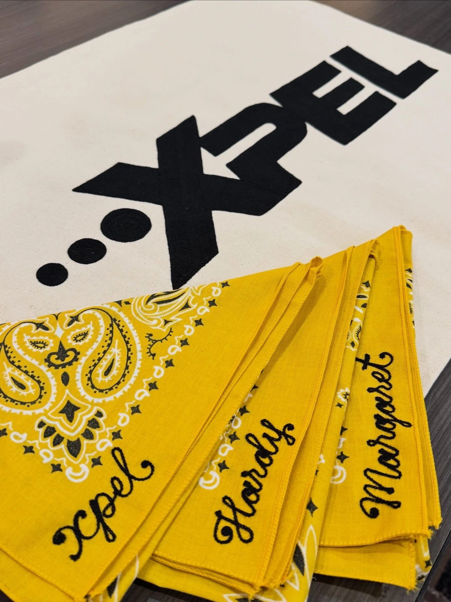 A white cloth with a black logo and three dots, and yellow bandanas with black text and a decorative pattern.
