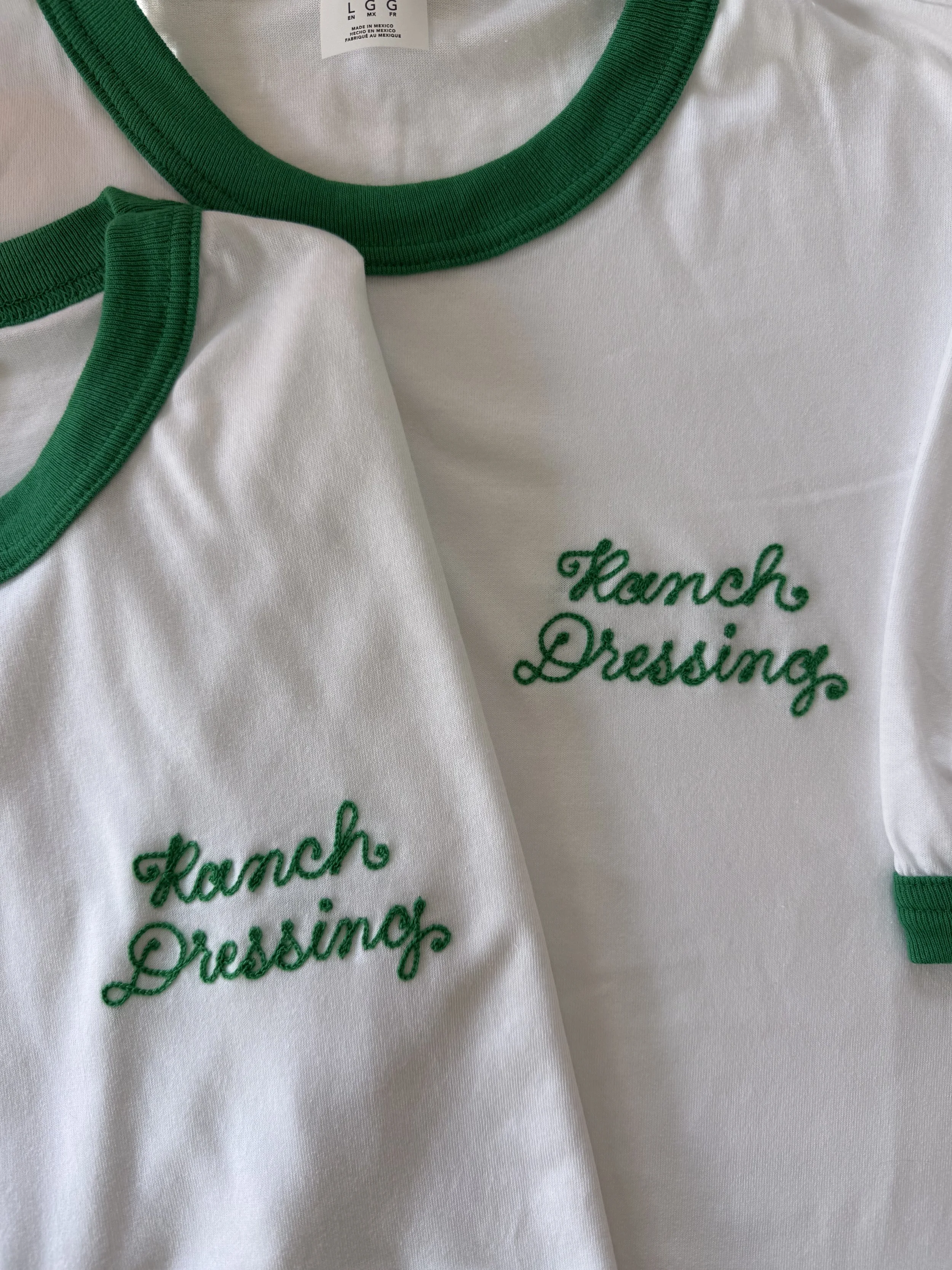 Two white t-shirts with green trim, embroidered with the words 'Ranch Dressing' in green chainstitched cursive. Activation support for SXSW. Brand ambassador uniforms for activations in Texas.