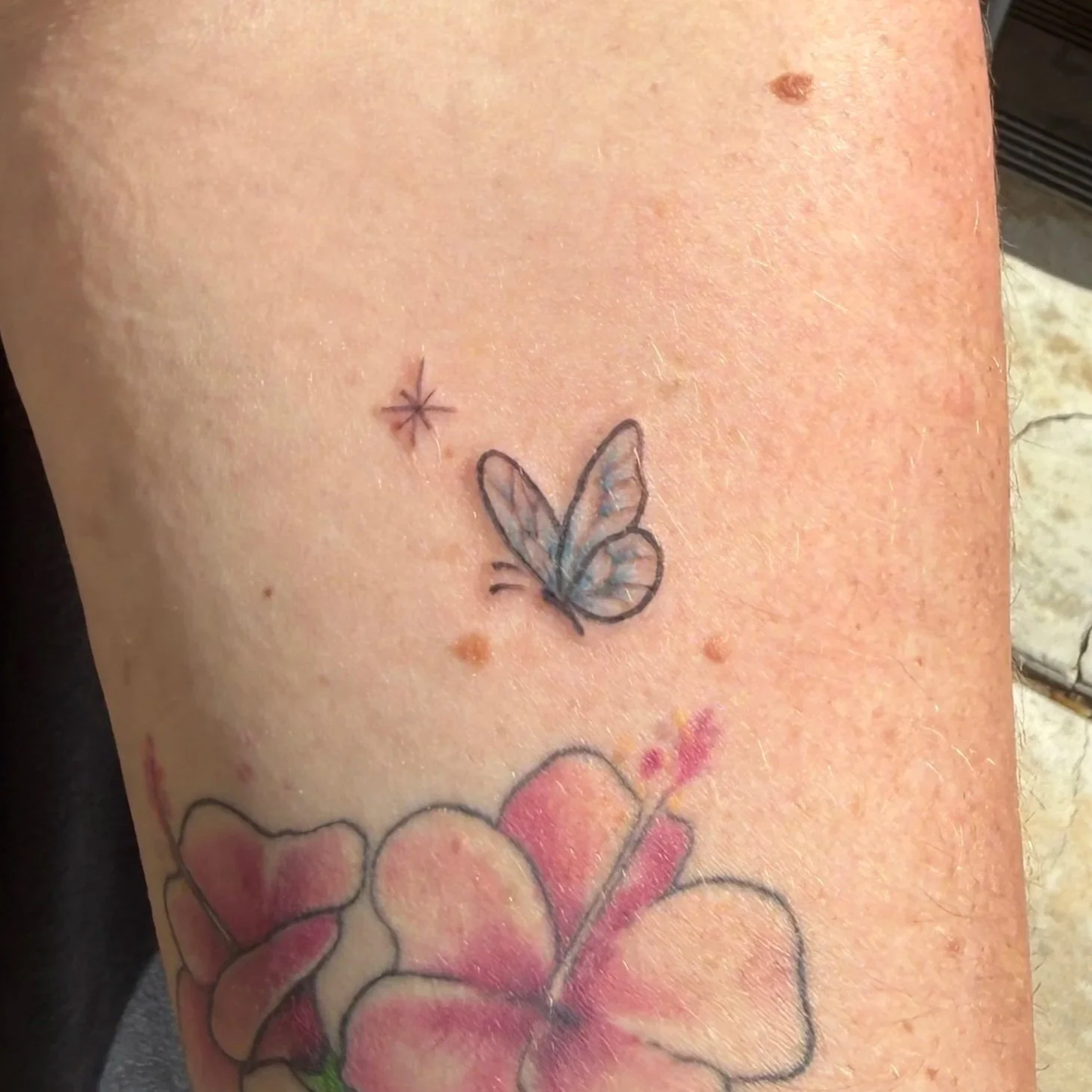 Close-up of a person's skin with a tattoo of a butterfly and several freckles.