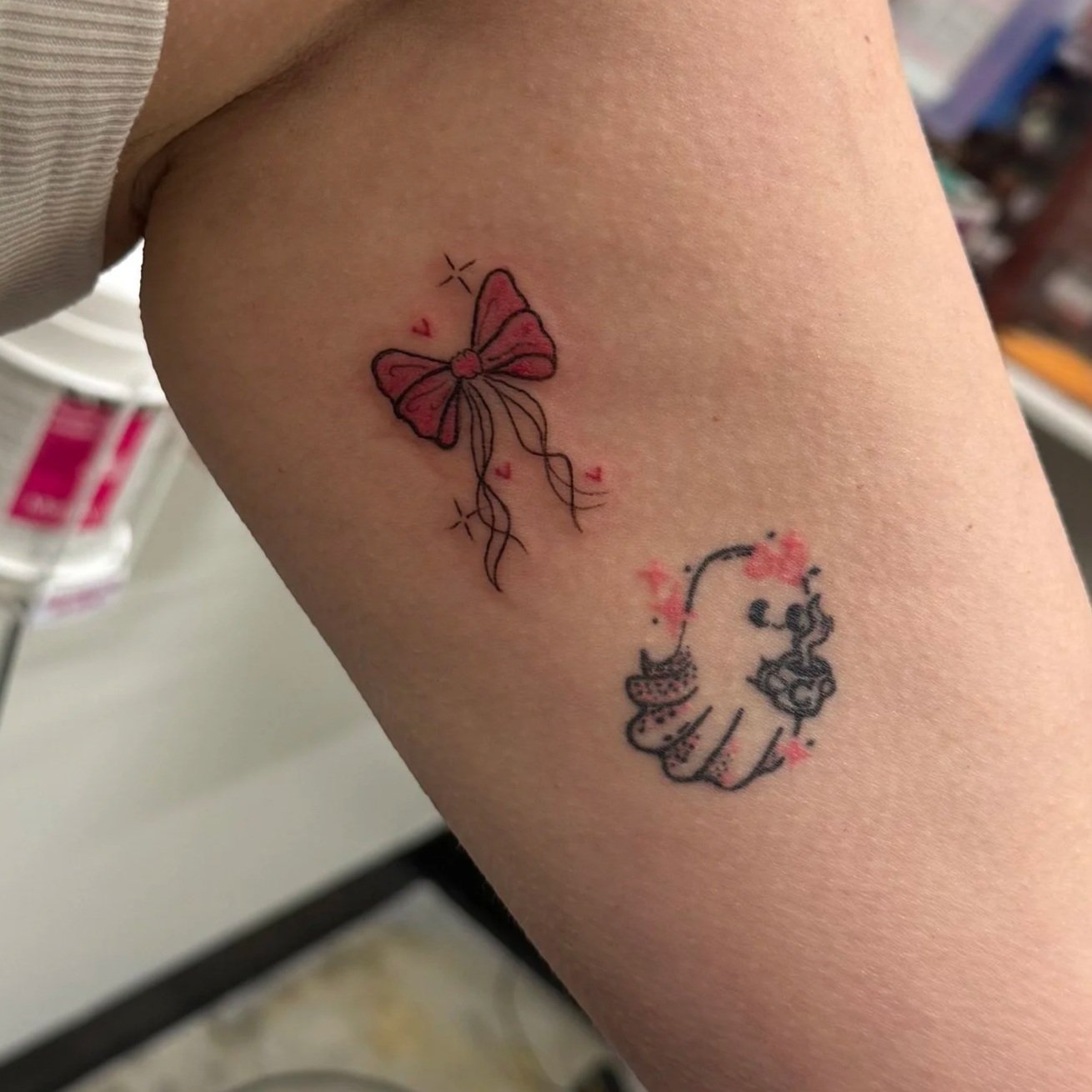 Tattoo of a pink butterfly with red and black accents, surrounded by small stars and hearts, on a person's arm.