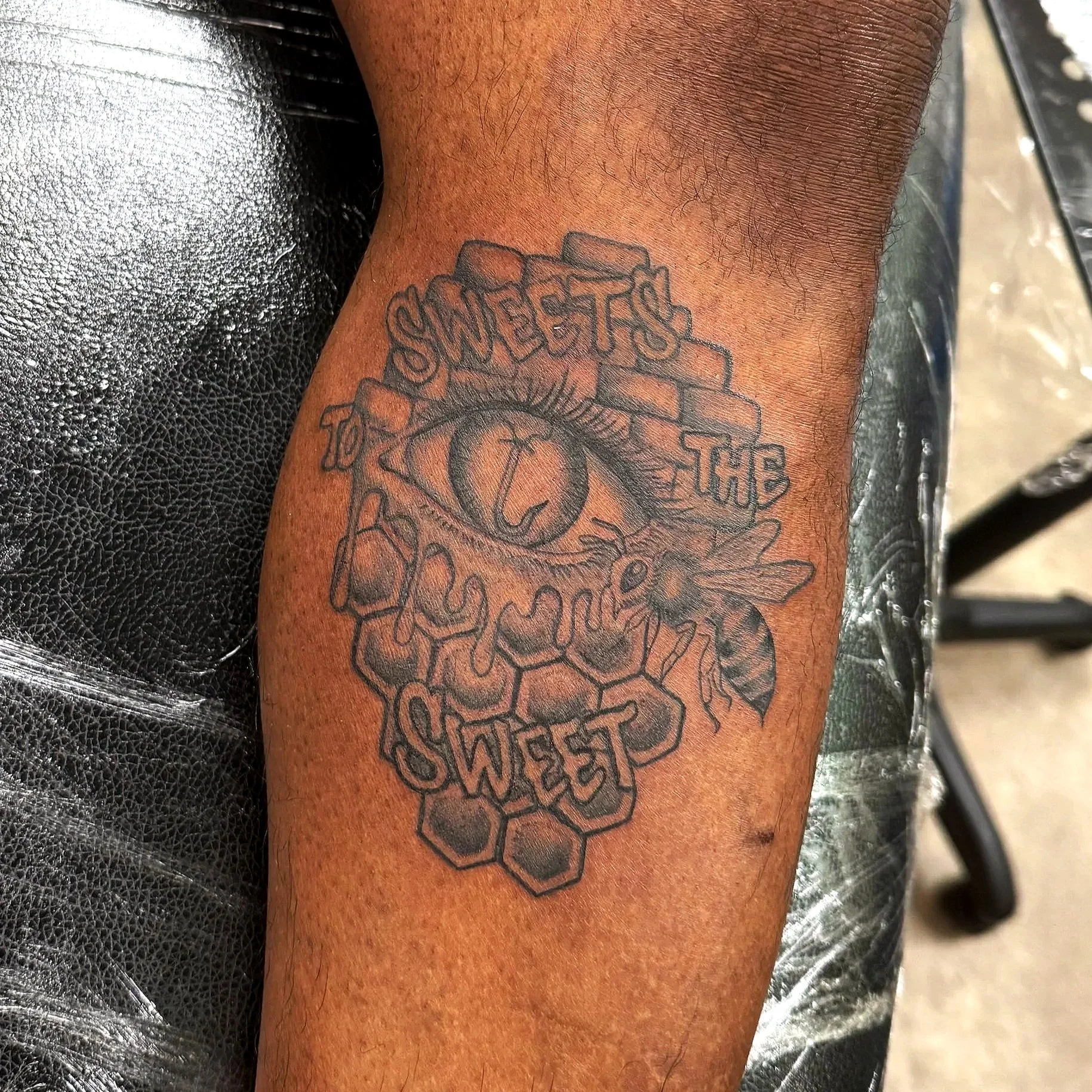 Tattoo on a person's arm with the words 'SWEETEST TO THE SWEET' surrounded by a honeycomb pattern.