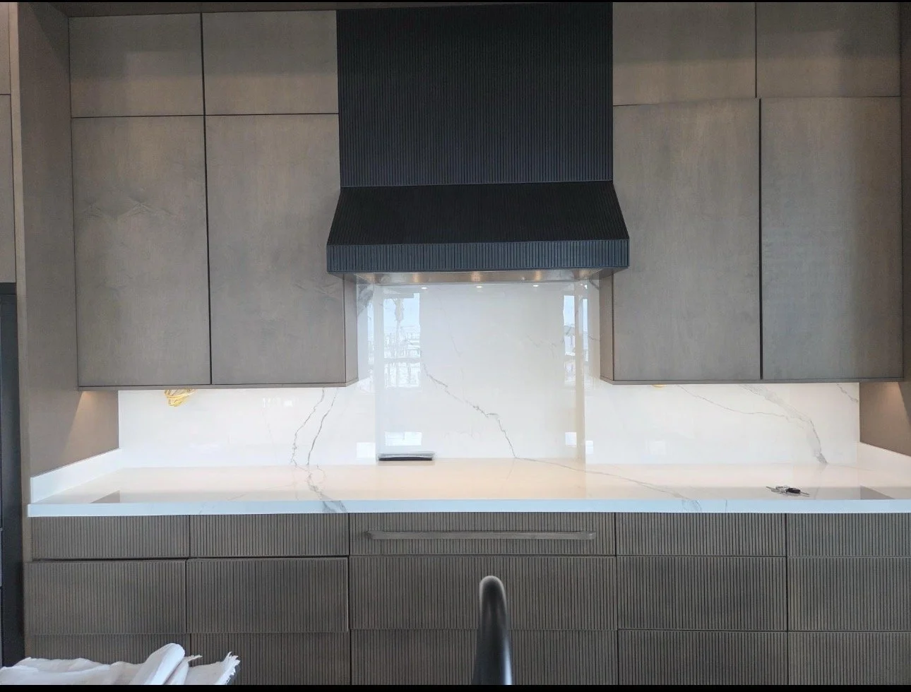 Modern kitchen with dark gray cabinets, a black range hood, and a white marble backsplash with gray veining.