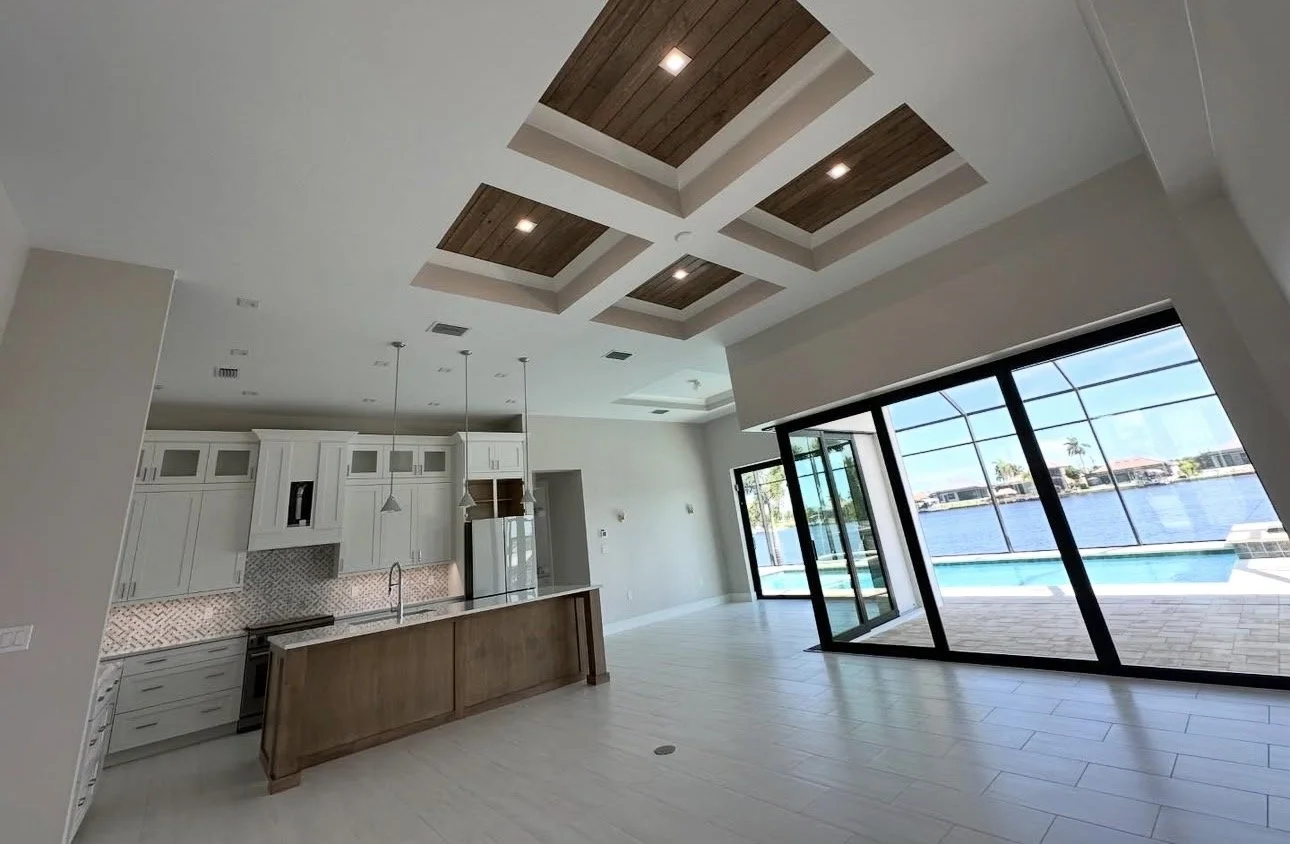Interior view of a modern, open-concept living space with a kitchen and large glass sliding doors leading to a patio and waterfront view.