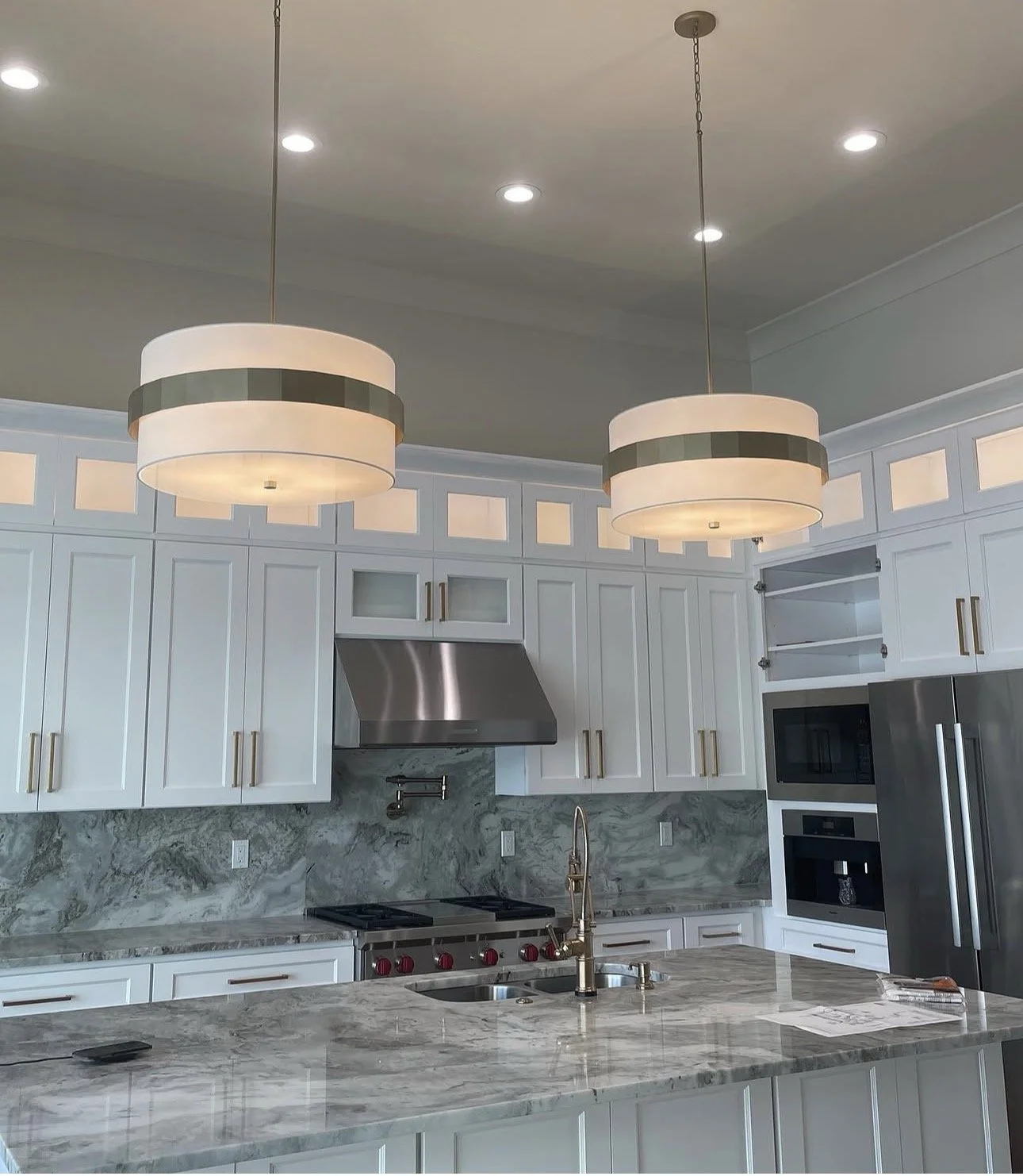 Modern kitchen with white cabinets, marble countertops, stainless steel appliances, and pendant lights hanging from the ceiling.