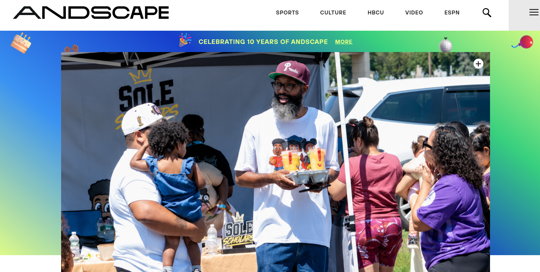 Man facing camera talking to a parent with a child in their arms in front of an event tent that says "Sole Scholars"