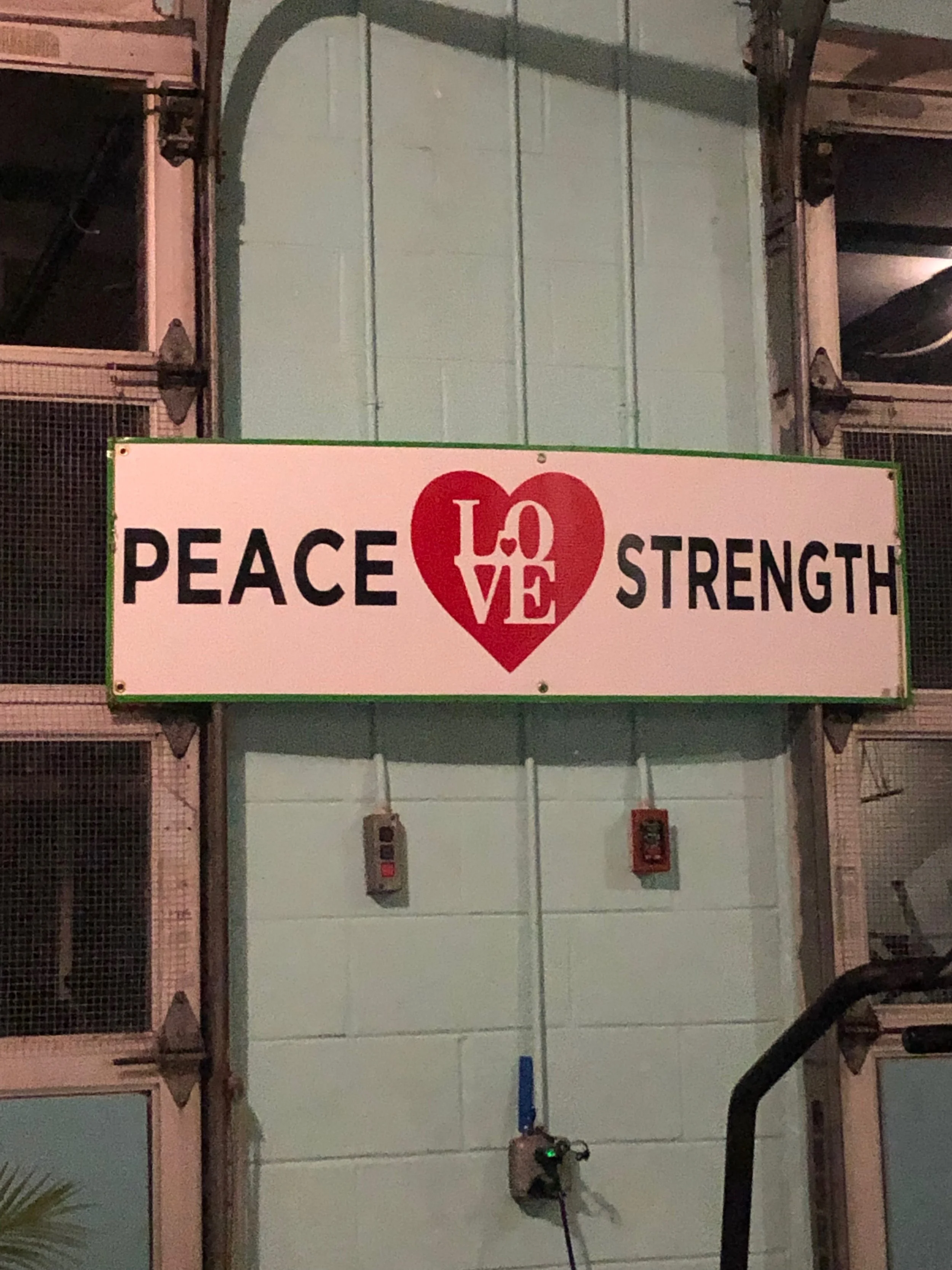 A sign on a light blue wall displaying the words PEACE, LOVE in a red heart, and STRENGTH.