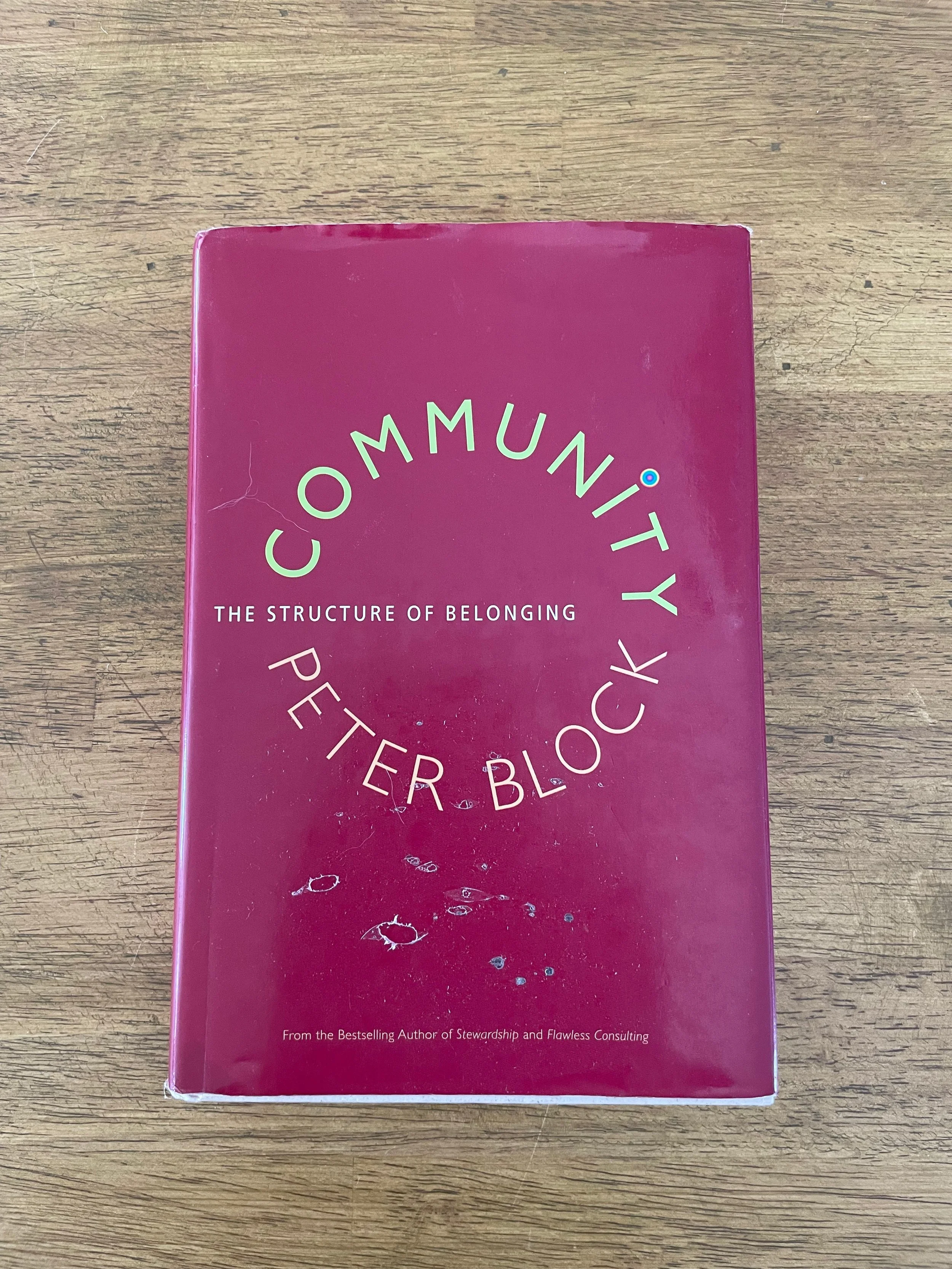 A red book titled 'Community' with the subtitle 'The Structure of Belonging' by Peter Block, placed on a wooden surface.