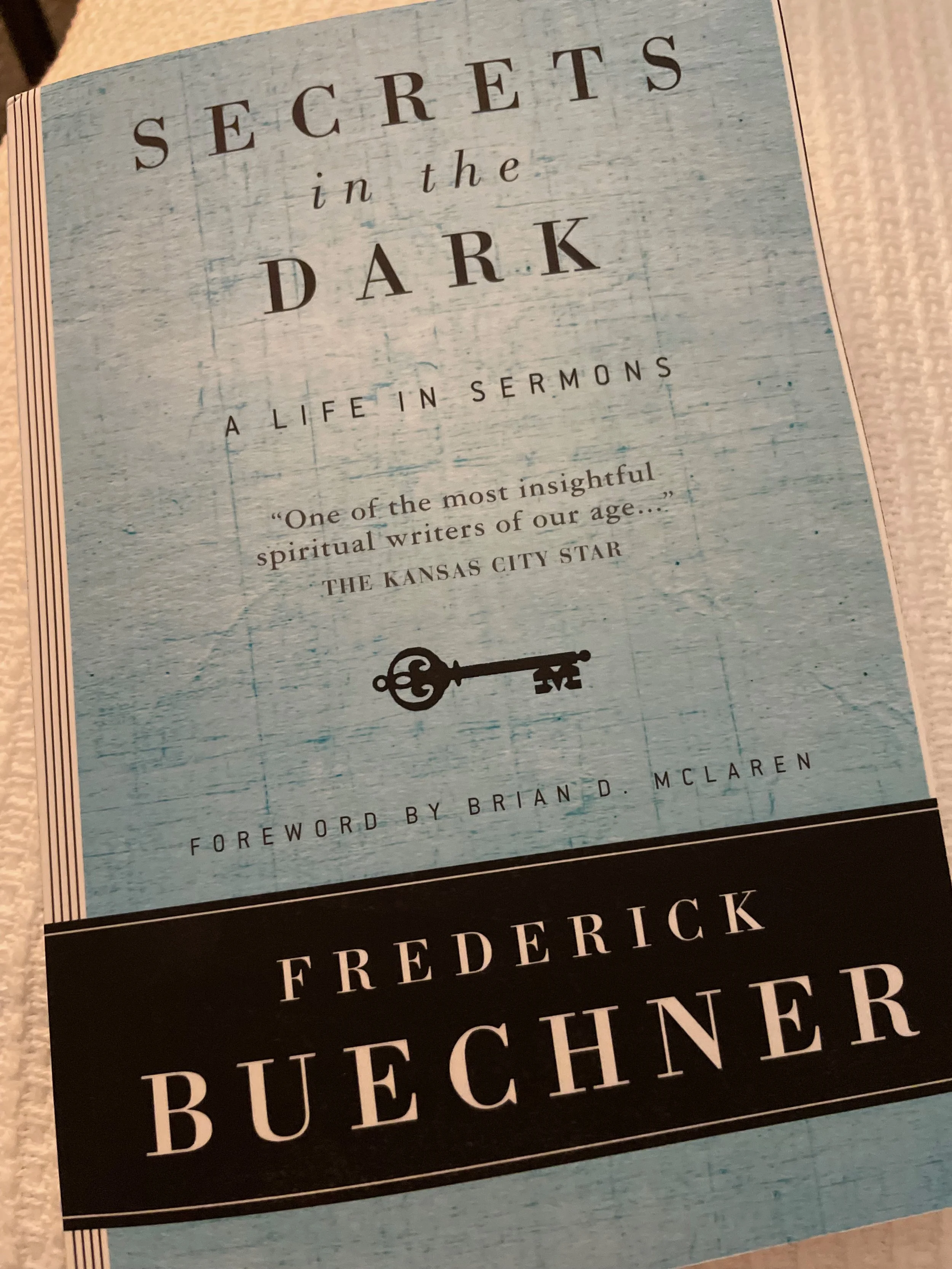 Book cover of 'Secrets in the Dark: A Life in Sermons' by Frederick Buechner, with a light blue background and black and white text, including a small illustration of a key.