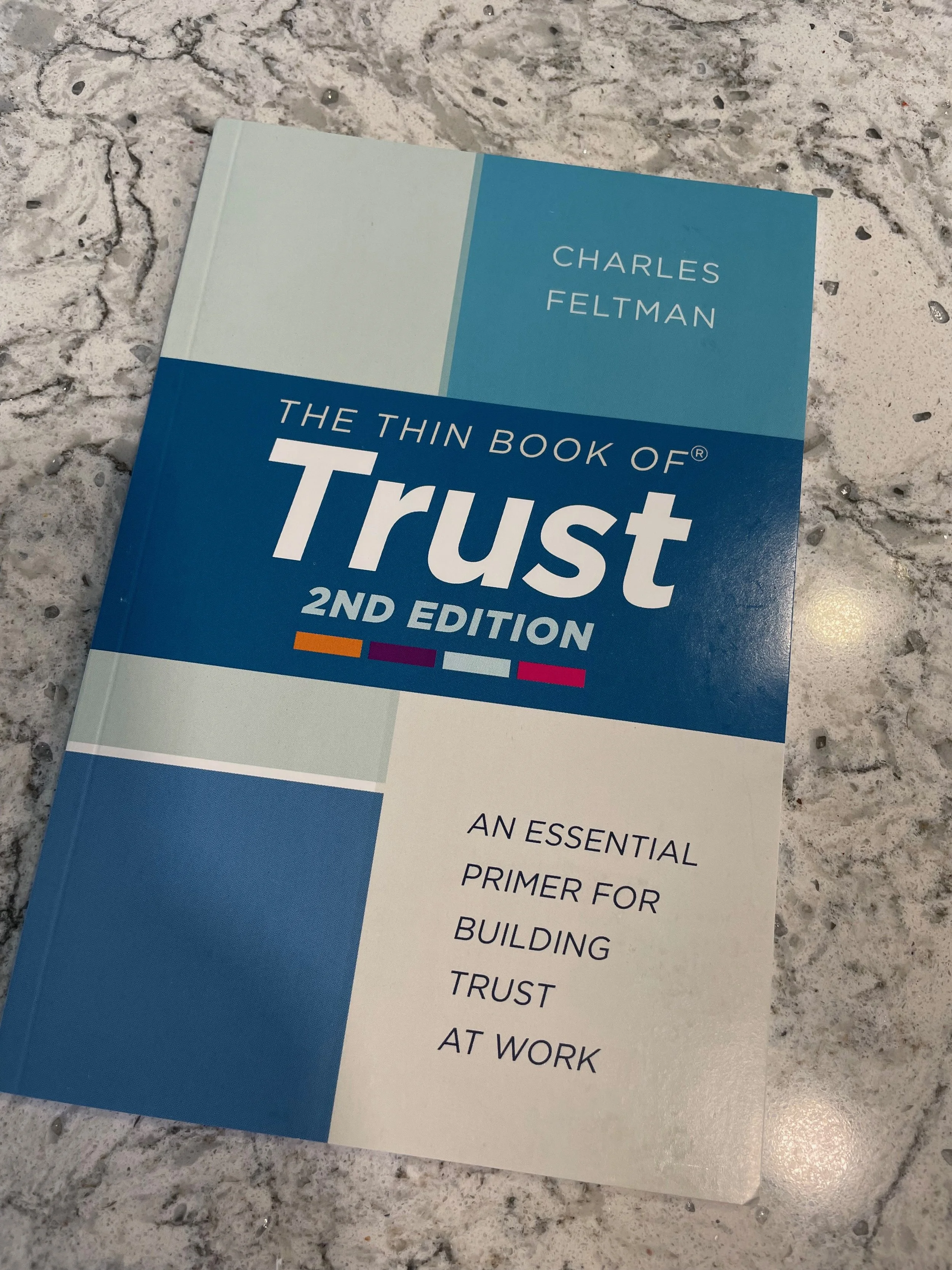 A book titled "The Thin Book of Trust" by Charles Feltman lying on a speckled granite countertop.