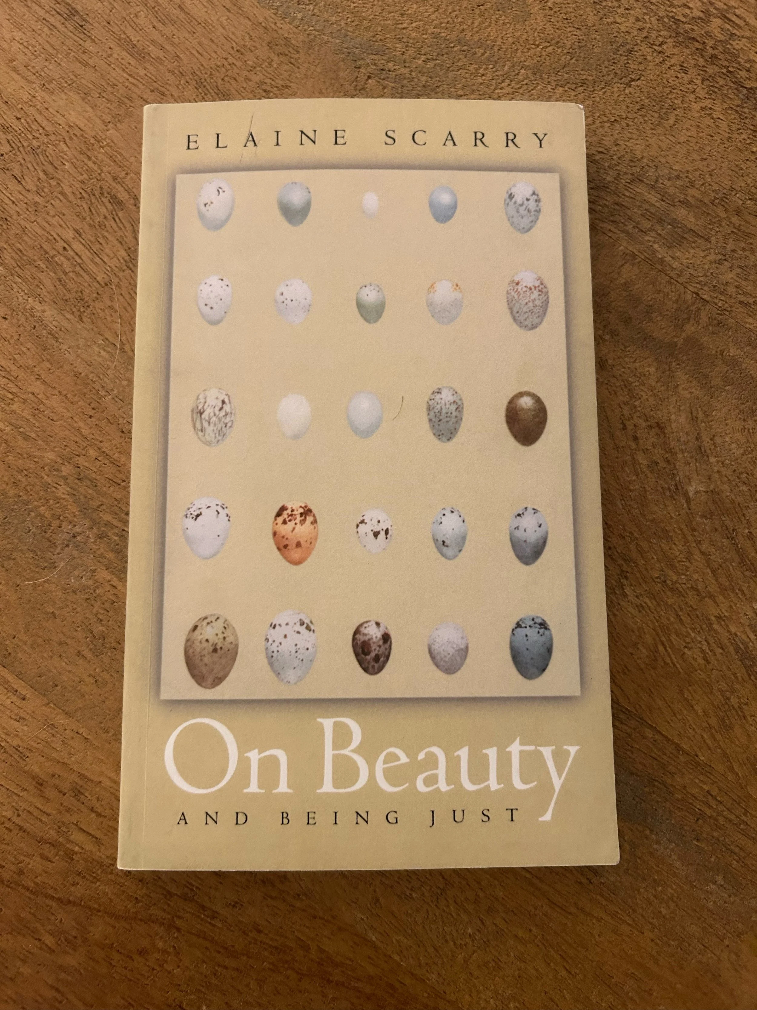 Book titled 'On Beauty and Being Just' by Elaine Scarry with a cover featuring various eggs with different speckled and patterned designs on a wooden surface.
