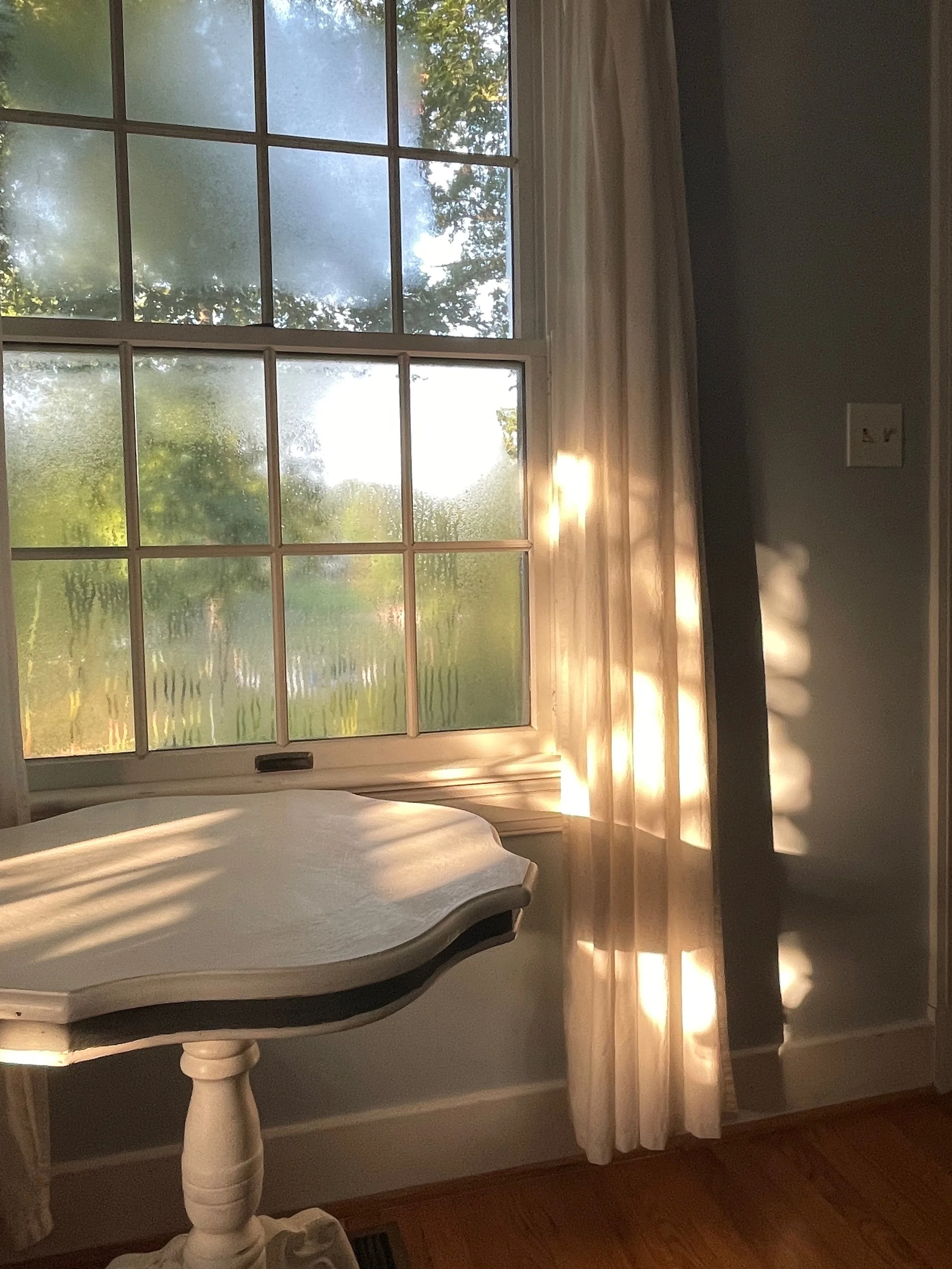 Sunlight reflecting off a window with sheer curtains, casting shadows inside a room.