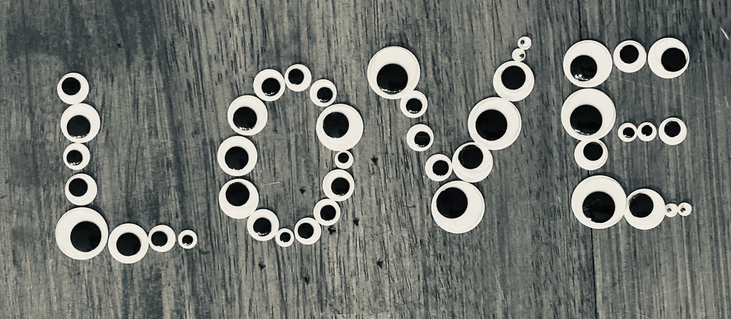The word 'LOVE' spelled out on a wooden surface with circular stickers featuring black and white eyes for each letter.
