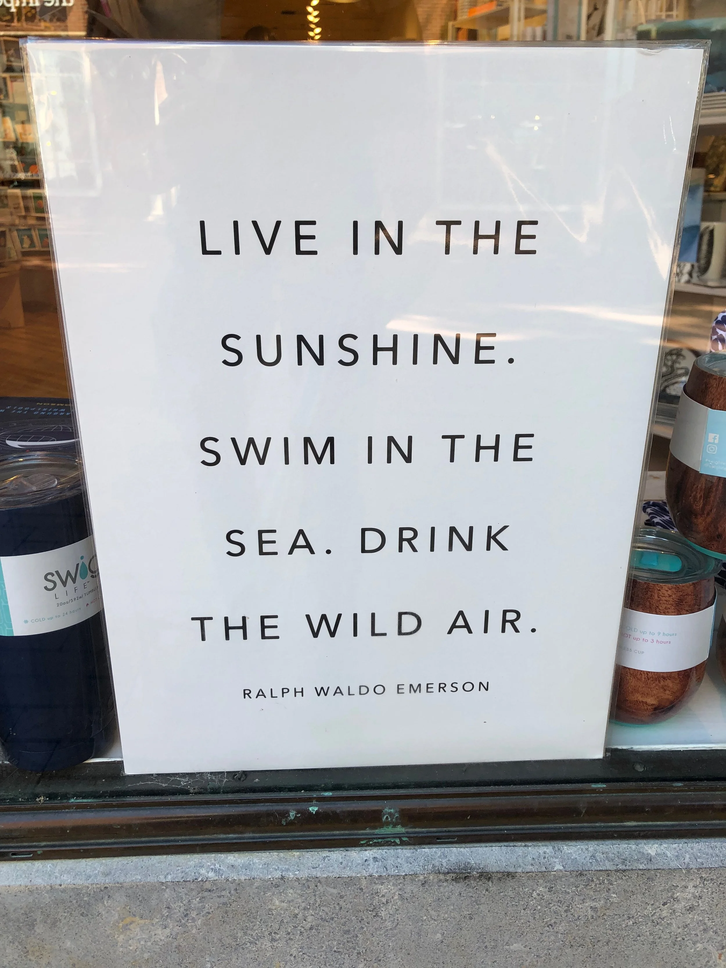 A white sign with black text quotes Ralph Waldo Emerson about enjoying sunshine, sea, and wild air.