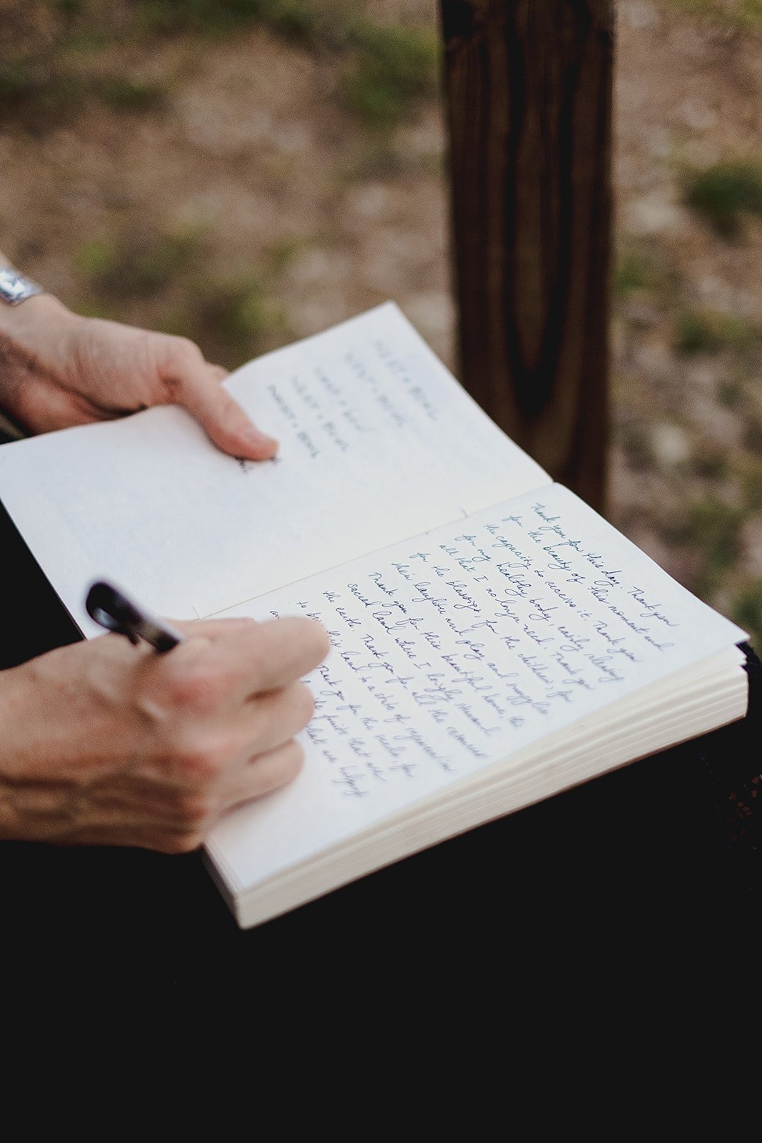 A person writing in a notebook outdoors, with handwritten text visible on the pages.