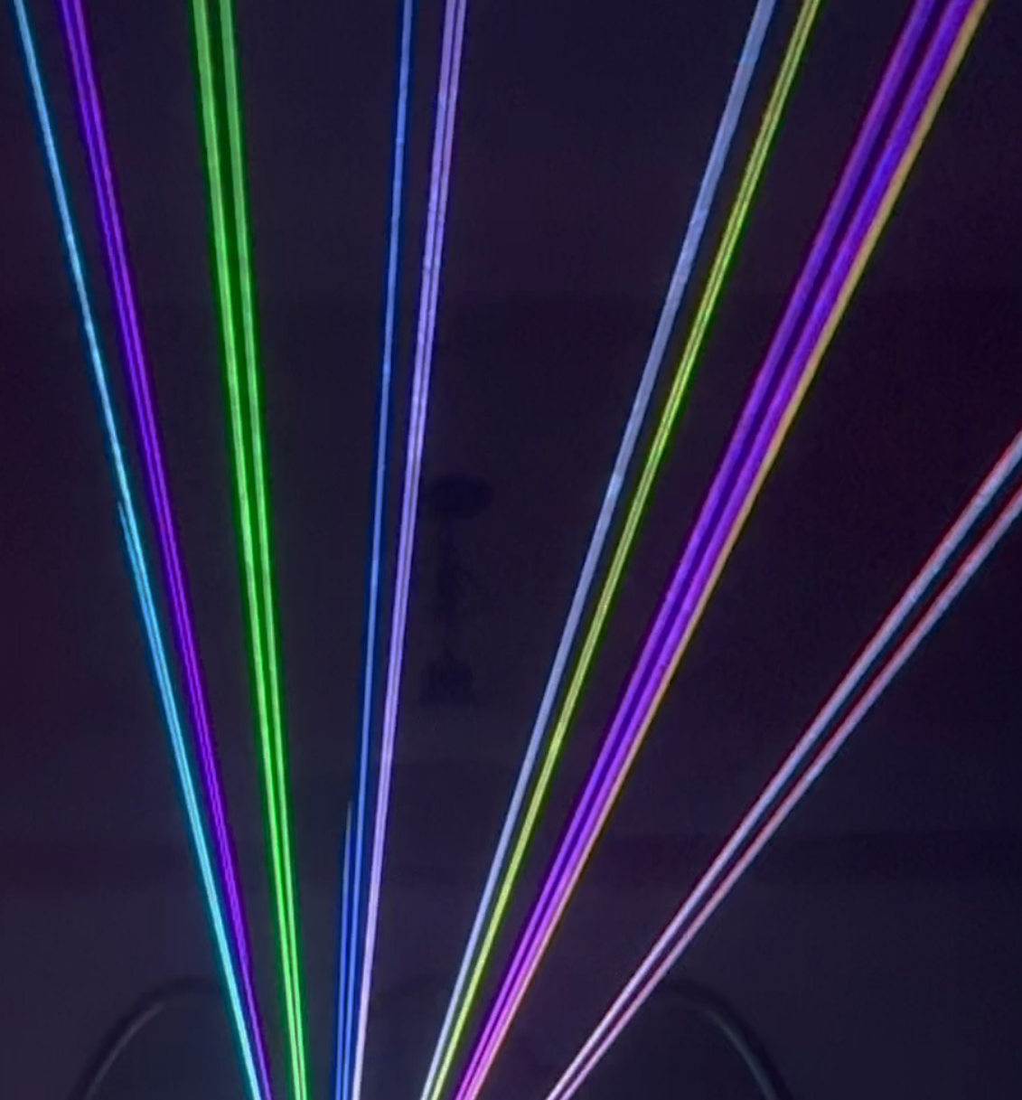 Multiple colorful laser beams in green, purple, blue, red, and violet projecting onto a dark ceiling or wall.