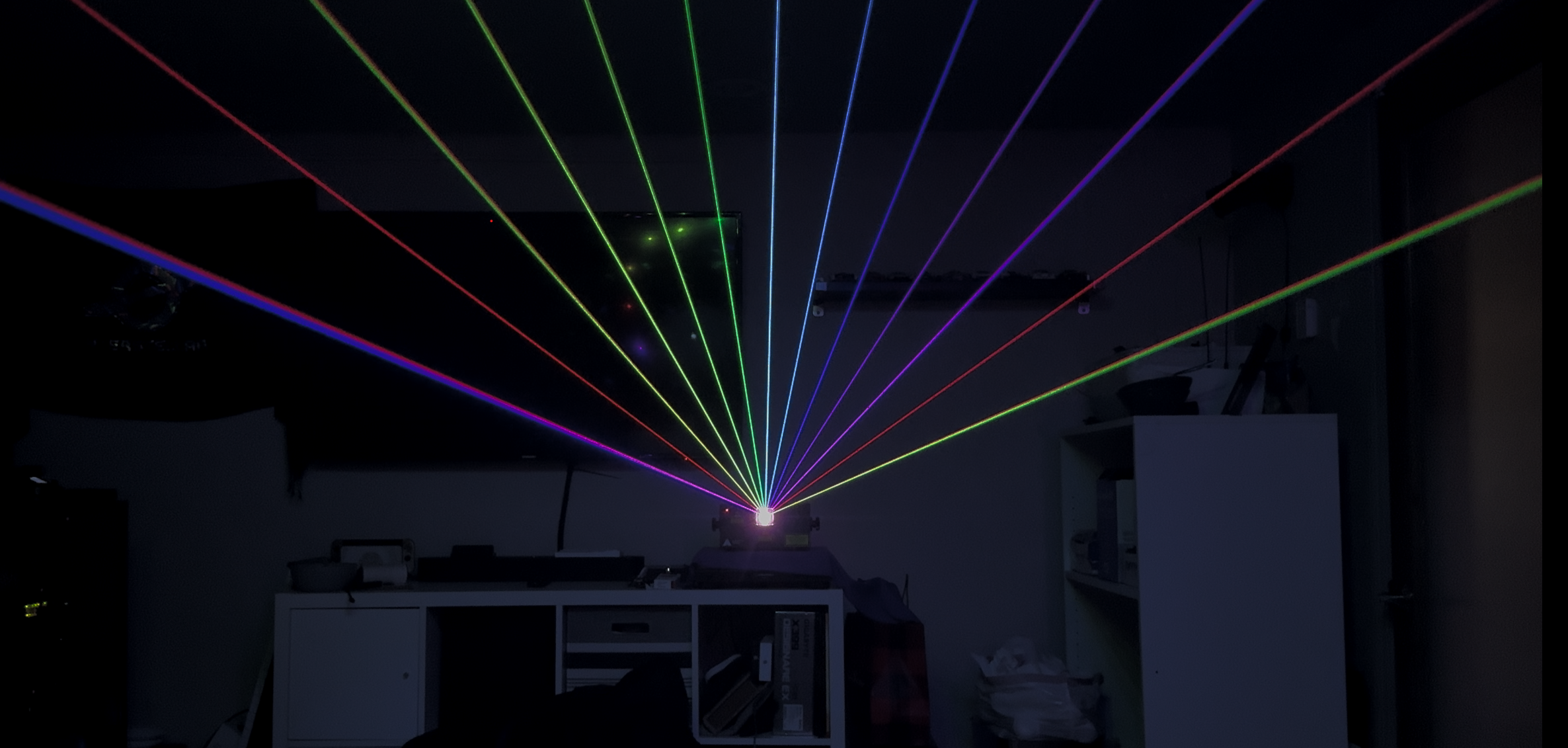 Color laser light beams projecting from a device in a dark room.
