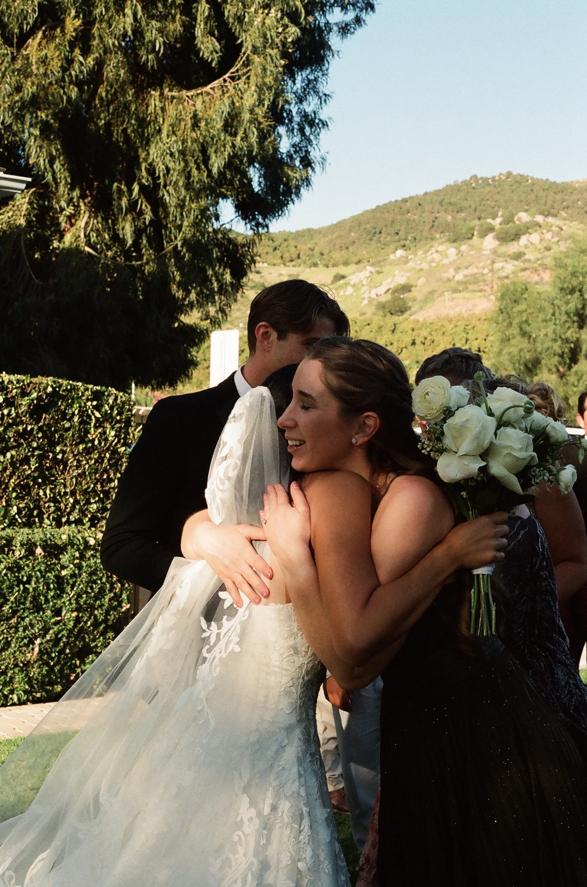 A bride and groom hugging during a wedding celebration outdoors with a scenic mountain background.