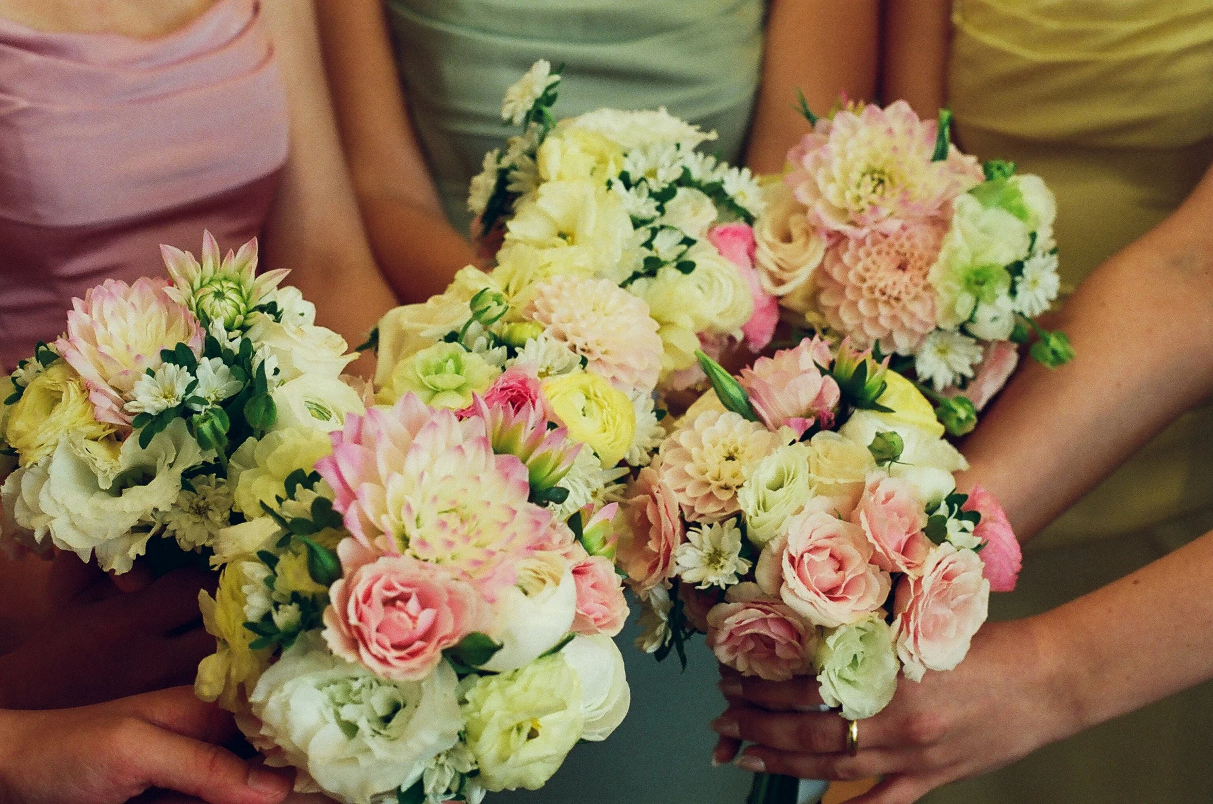 Three people holding Bundles of mixed pink, white, and yellow flowers in their arms.