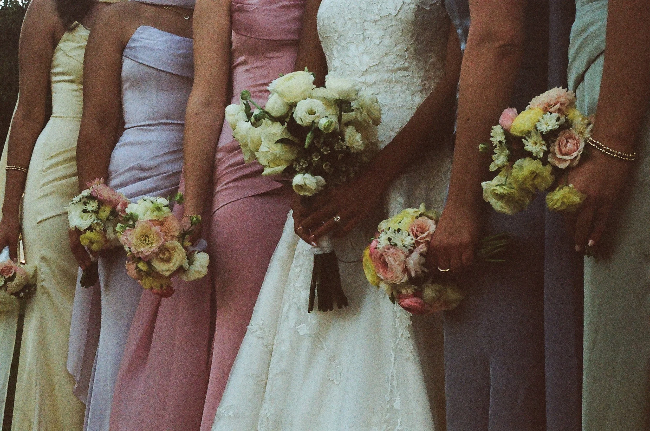 Several women dressed in colorful coordinated dresses holding bouquets of flowers, likely at a wedding or special event.