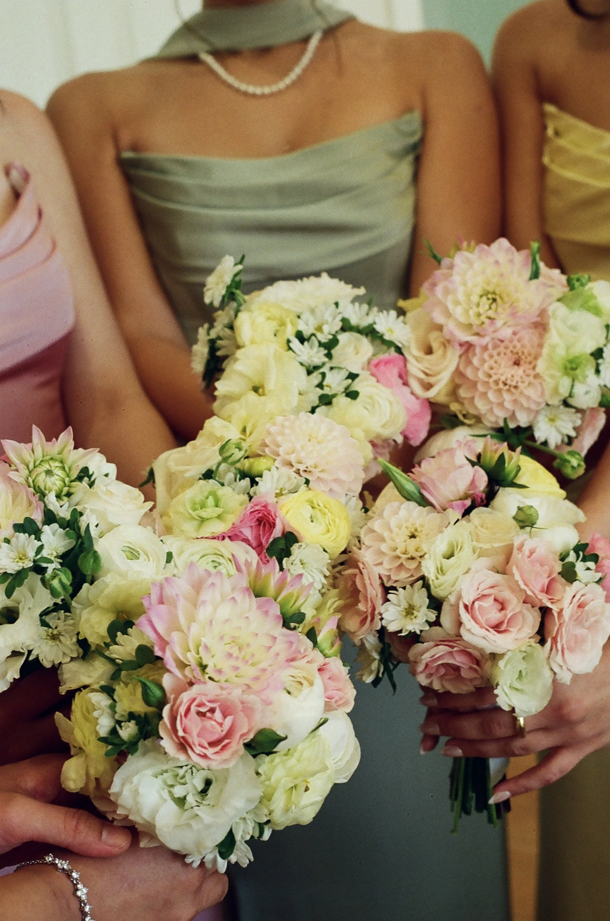 Three women holding bouquets of pastel-colored flowers, wearing elegant dresses, at a formal event or celebration.