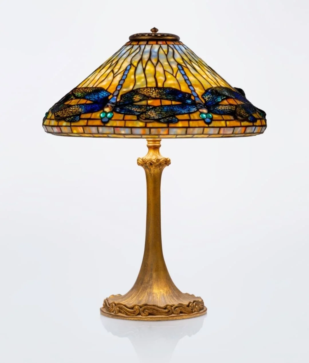 A decorative table lamp with a stained glass shade featuring dragonflies and blue beads, and a gold-colored ornate base.