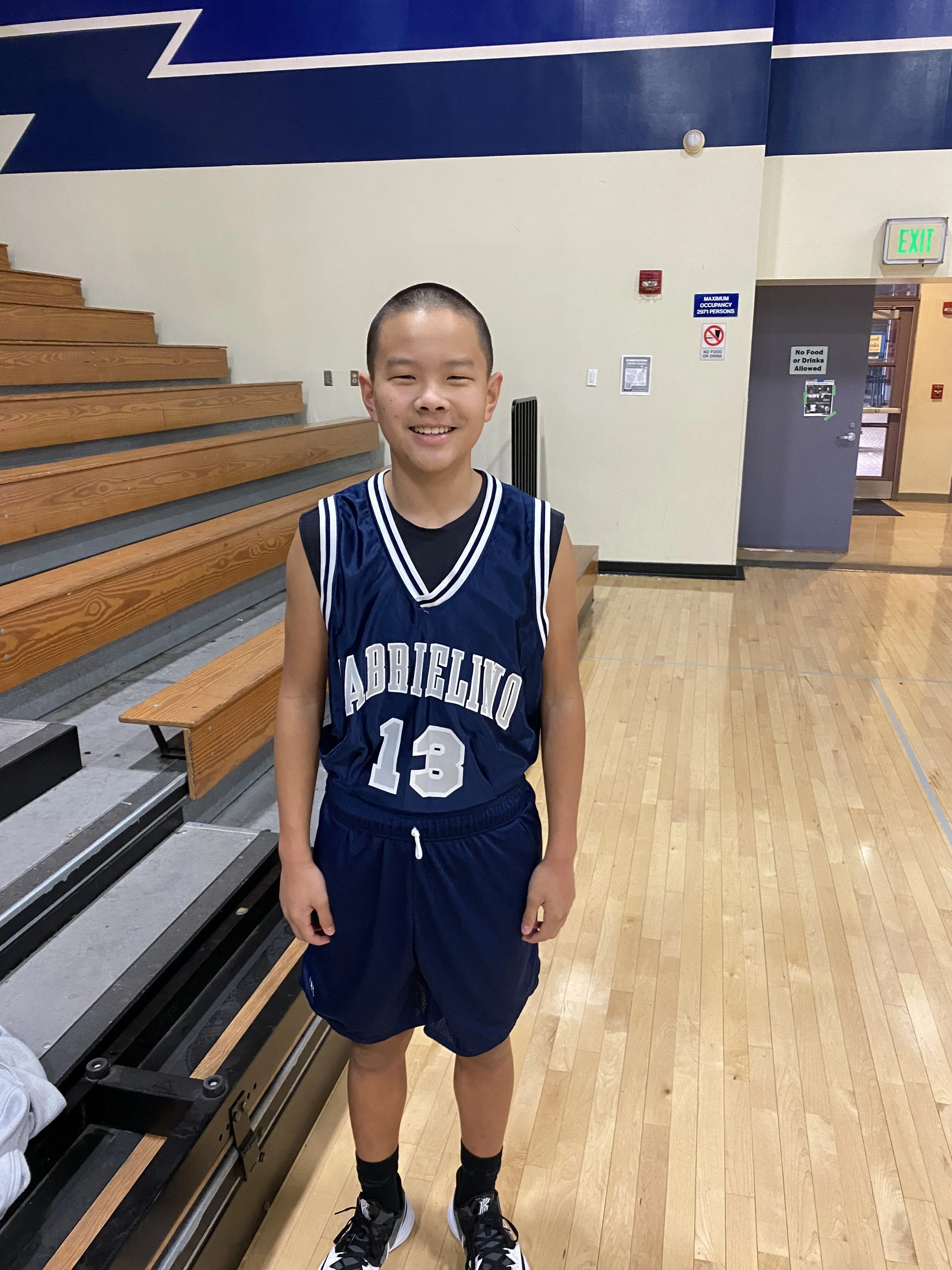 Young basketball player in jersey number 13 standing in a gym