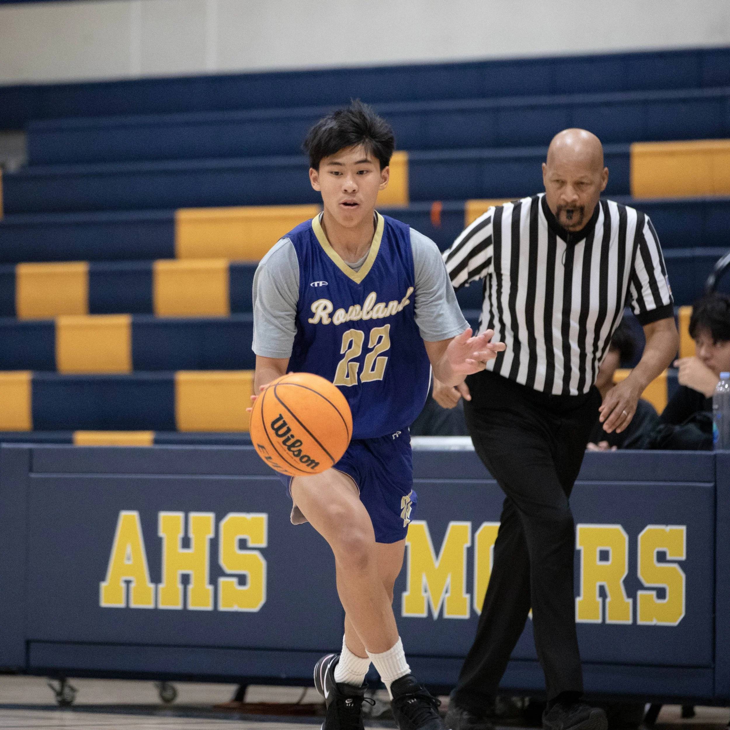 Basketball player in Rowland jersey dribbling with referee nearby.