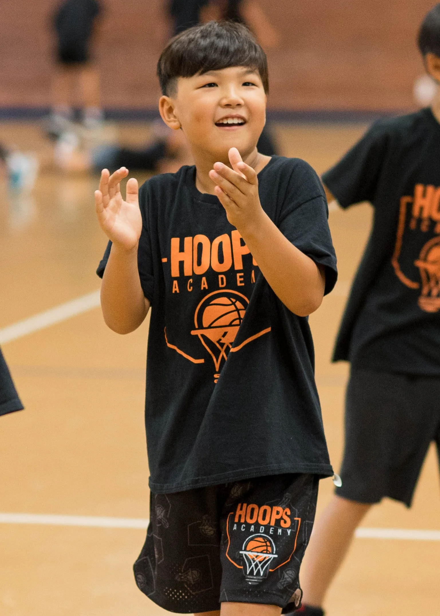 Young boy in a basketball jersey with a medal, standing on a basketball court.