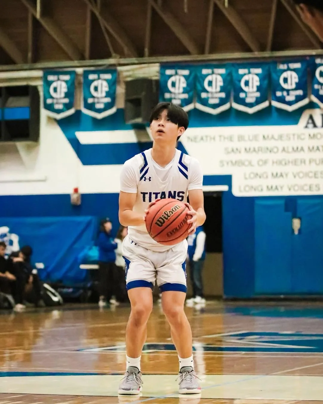 Basketball player in white "Titans" jersey preparing to shoot a free throw in a gym with banners in the background.