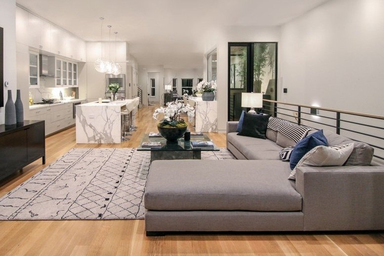 Modern open-plan living room and kitchen with gray sectional sofa, marble island, wood flooring, and decorative accessories.