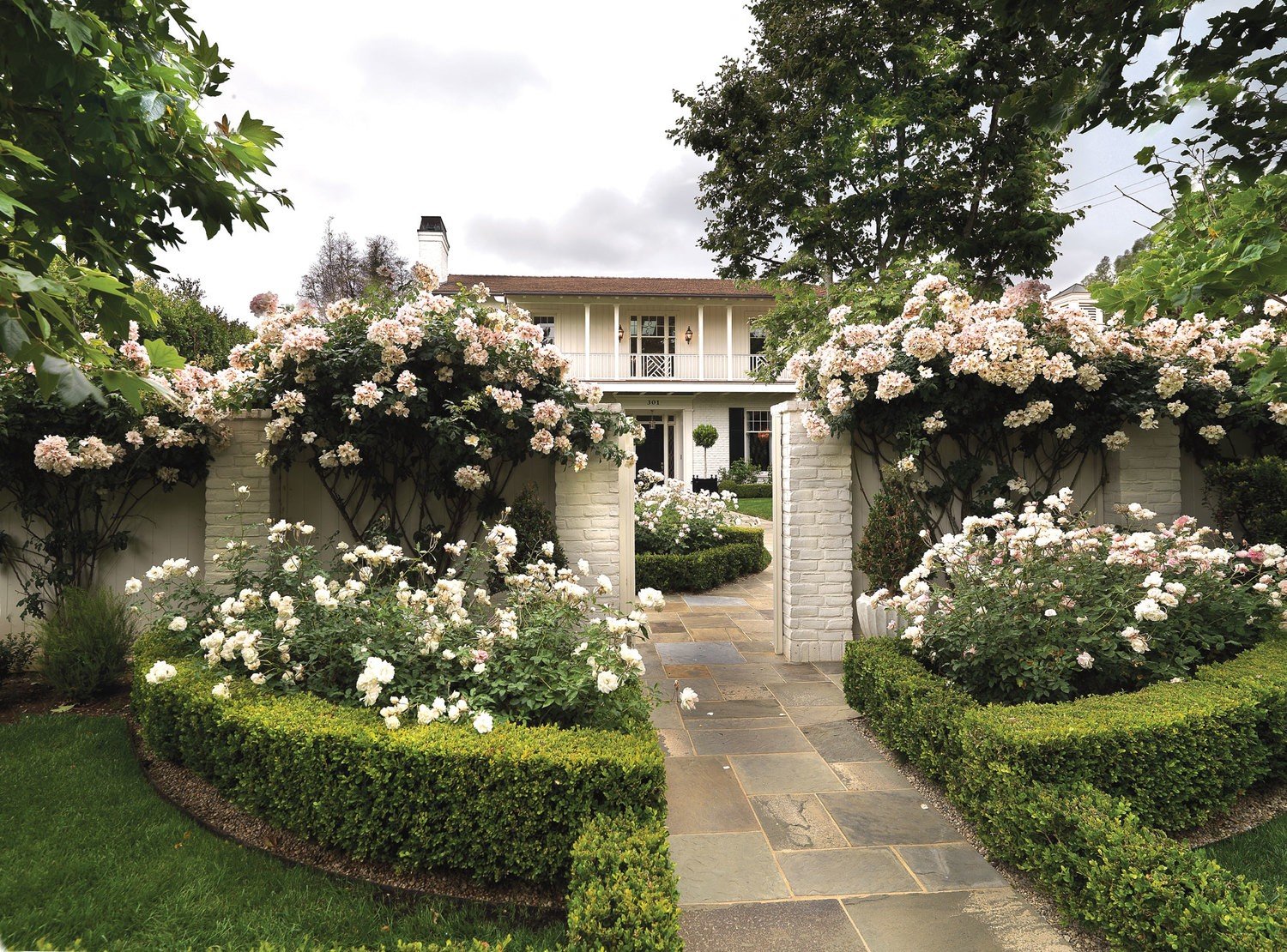This custom Brentwood Park home has a privacy wall with lush greenery and blooming white roses, creating a beautiful entrance.