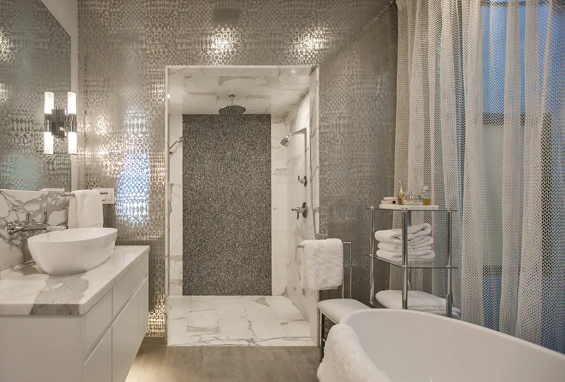 Modern bathroom with a metallic wall design, marble sink countertop, vessel sink, walk-in shower, freestanding bathtub, and towel shelf.