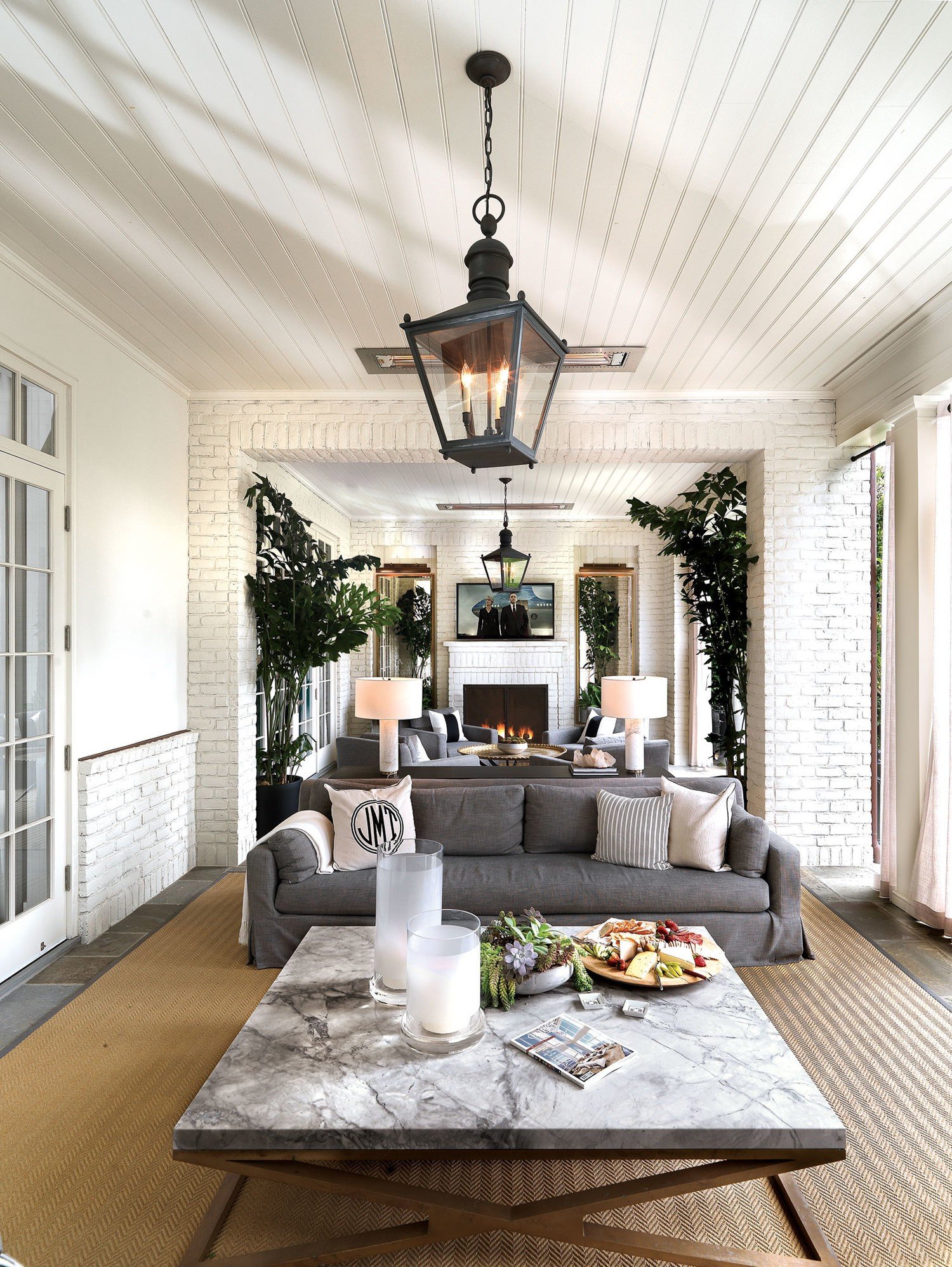 This cozy outdoor living room features white-paneled ceiling and white brick walls making the outdoor space feel just as luxurious as the inside.