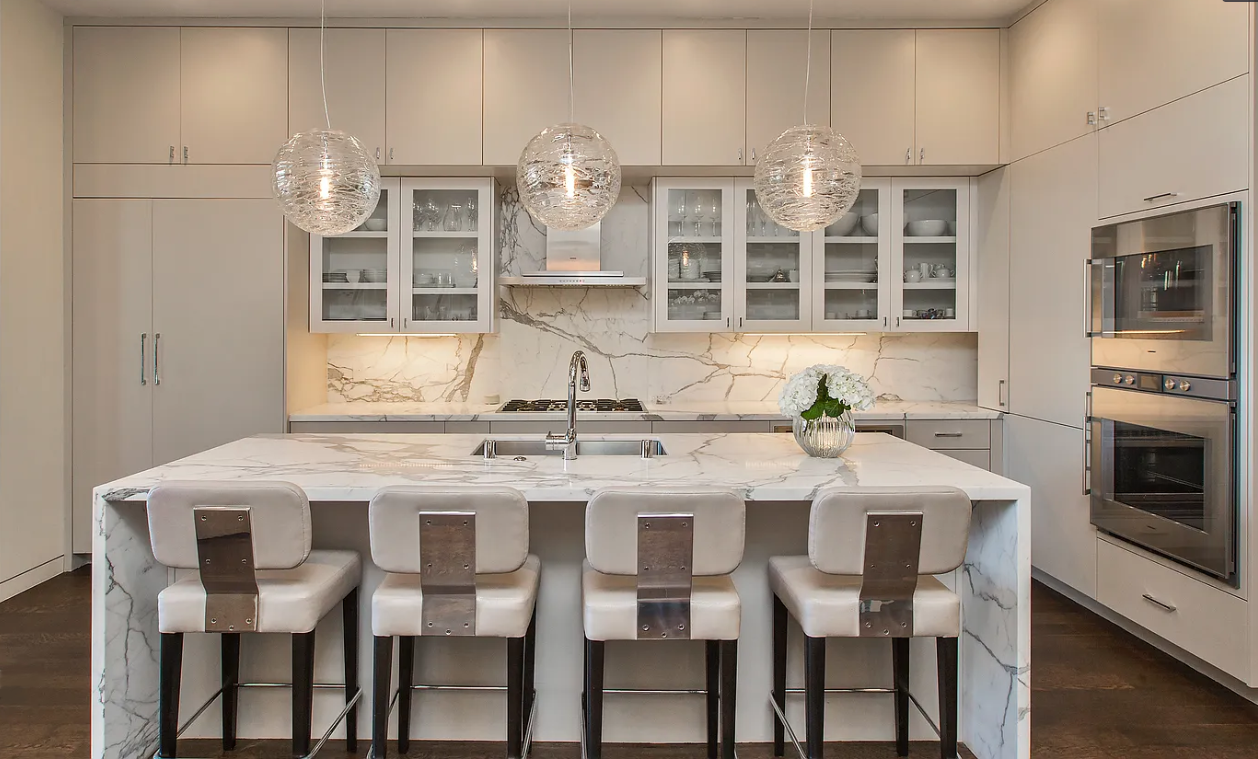 Modern kitchen with white cabinetry, marble island, pendant lighting, and stainless steel appliances.