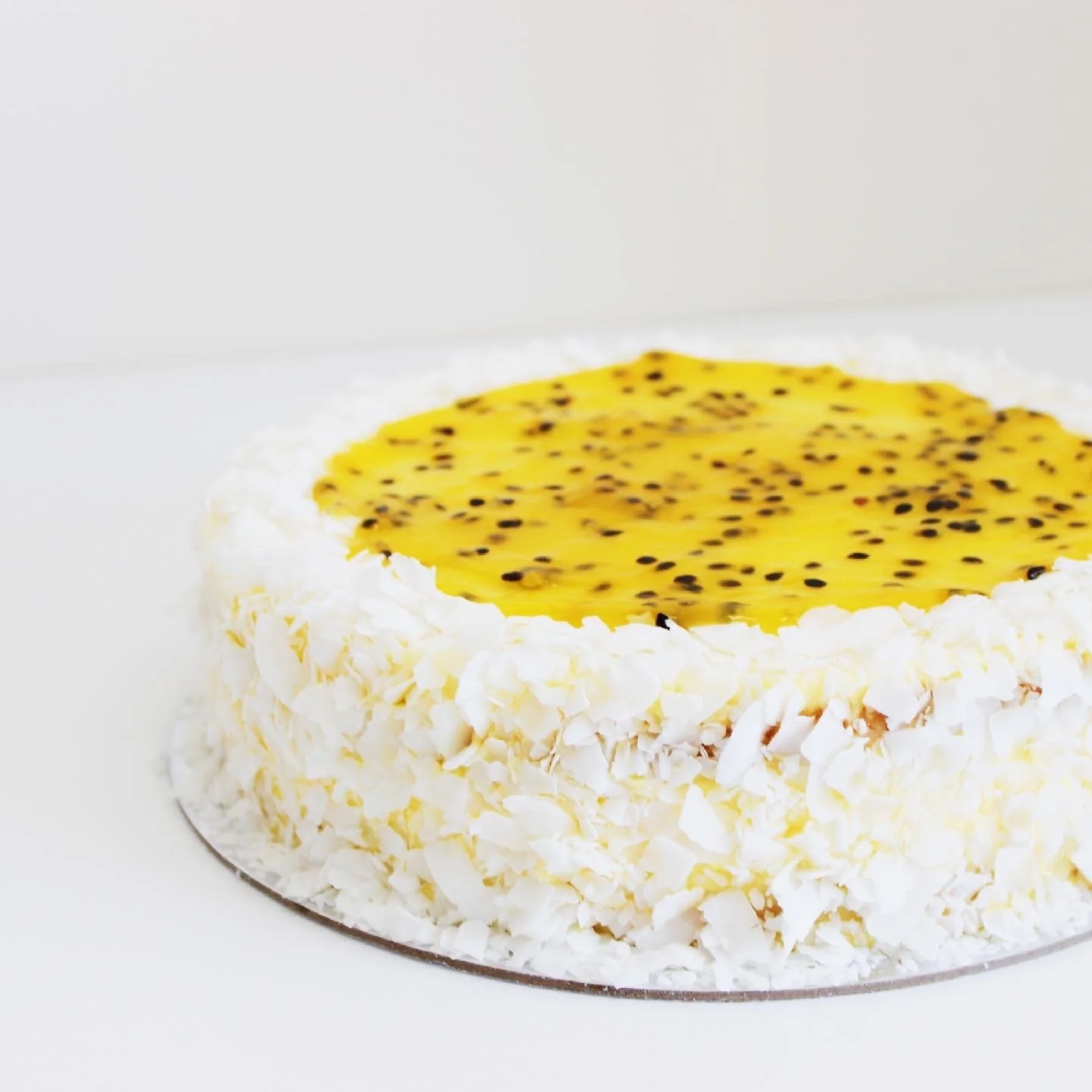 Passionfruit & mango mousse cake with white shredded coconut on the sides and a yellow passion fruit topping.