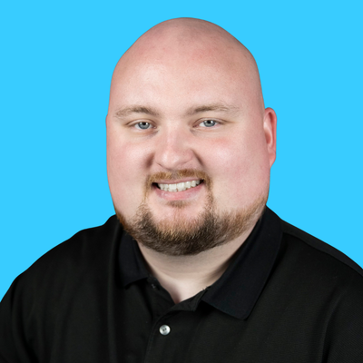 Headshot of a bald man with a beard smiling against a blue background.