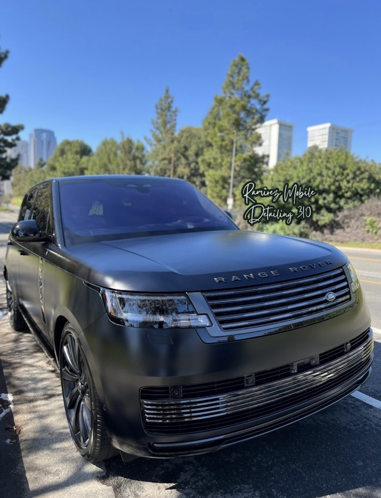 A black Range Rover parked outdoors on a sunny day with trees and buildings in the background.