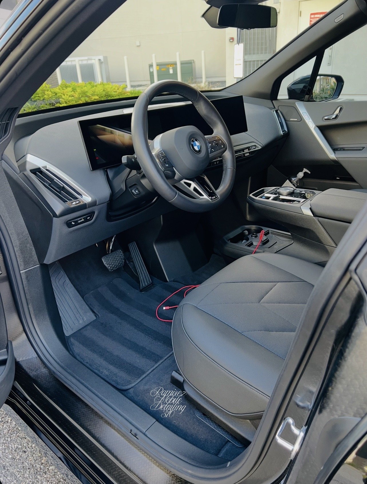 Interior of a modern BMW vehicle, showing the steering wheel, digital dashboard, center console with gear shifter, and gray seats.