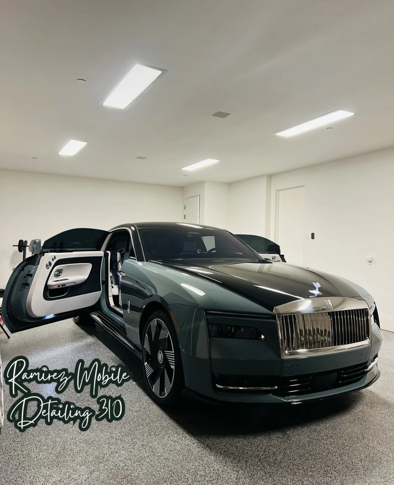 A luxury black and silver car inside a white garage with ceiling lights, with its passenger door open. The car has a sleek design and shiny finish.