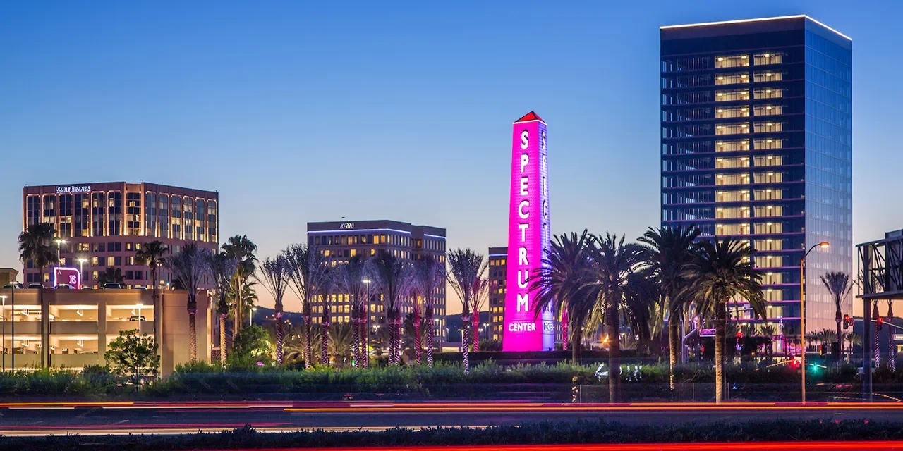 Nighttime cityscape with lit buildings, palm trees, and a pink neon sign that reads 'Spectrium Center' in Las Vegas.