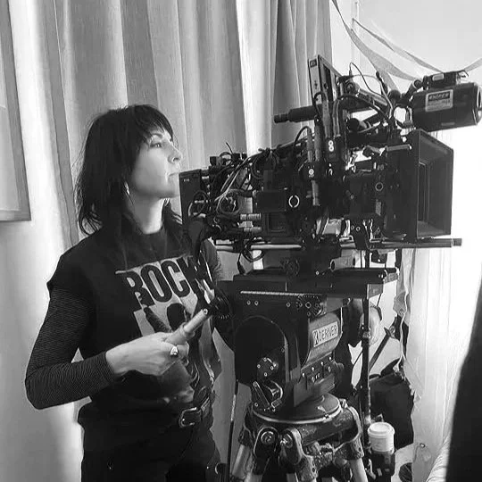A woman operating a professional film camera on a tripod in a room with curtains in Portland, Oregon.