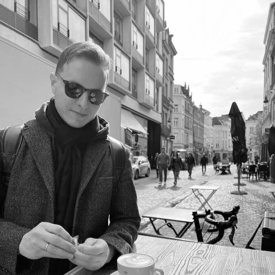 A man sits at an outdoor cafe table on a city street in Portland, Oregon with a coffee drink with latte art in front of him. 