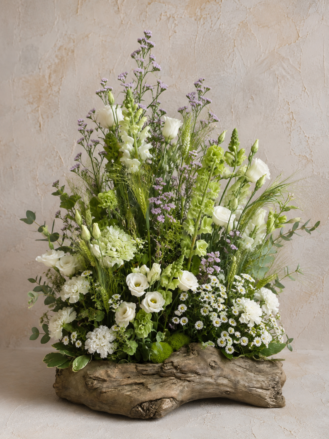 A floral arrangement with white and purple flowers in a rustic wooden container against a textured taupe background.