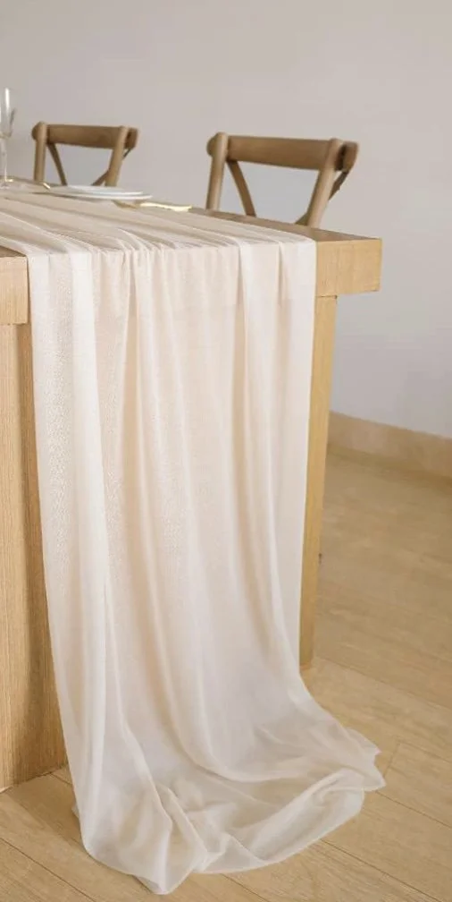 Cream-colored curtain draped over the edge of a wooden table in a dining area with wooden chairs and a light-colored floor.